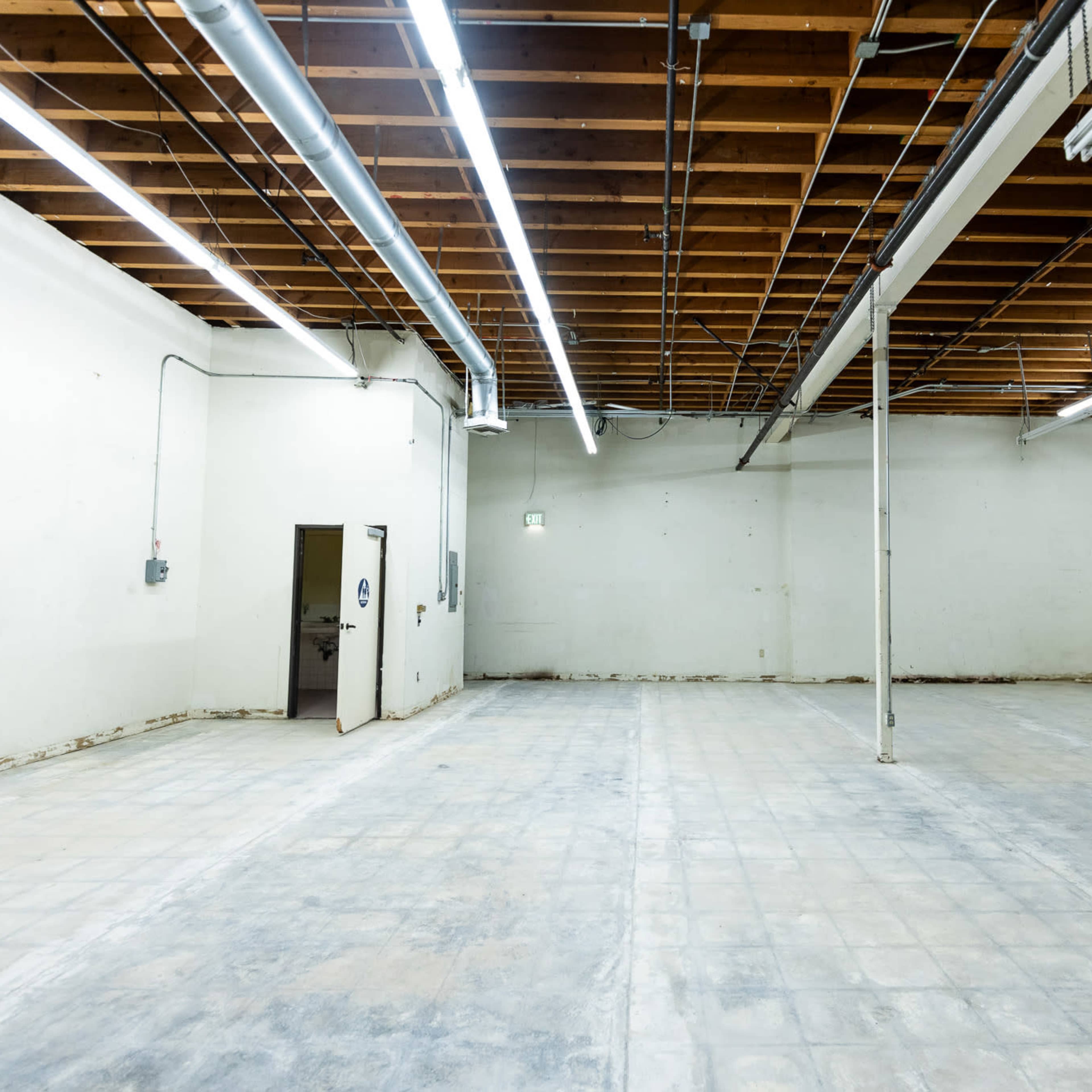A spacious, empty room with bare walls, a concrete floor, and exposed wooden beams overhead.