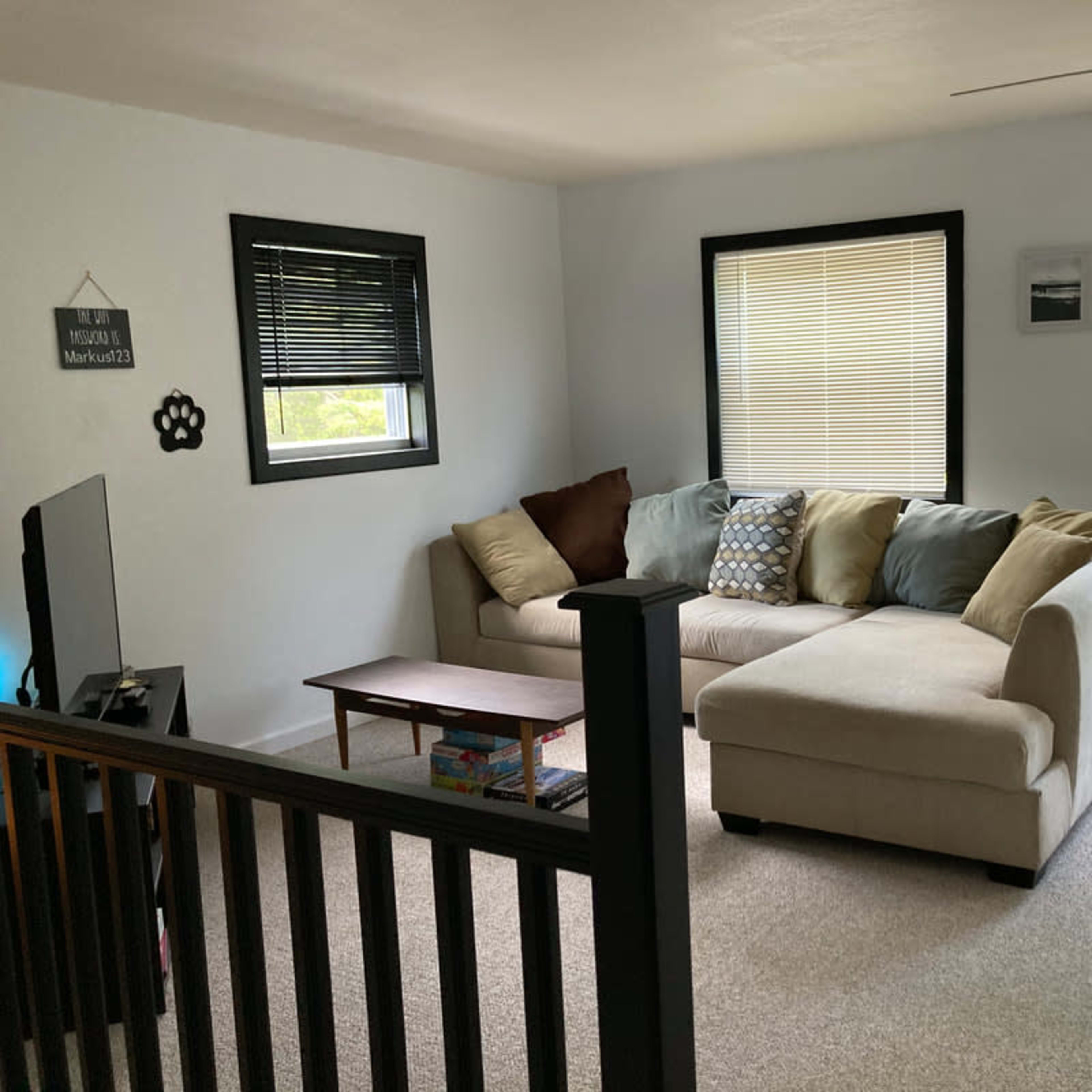 A light-filled living room features a sectional sofa, a coffee table, a TV, and a door leading to an outdoor space.