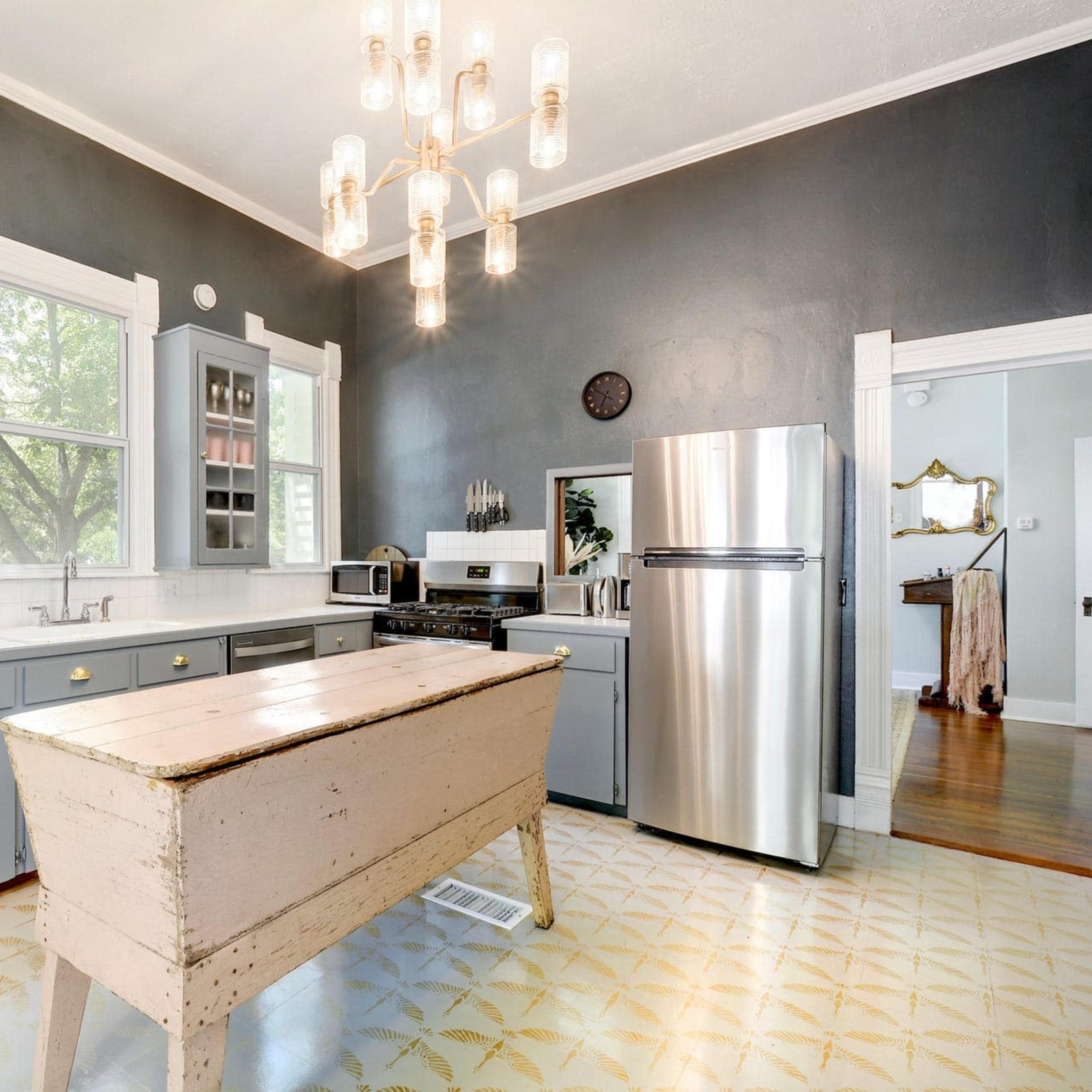 A modern kitchen features gray cabinetry, stainless steel appliances, and a large wooden island illuminated by a chandelier.