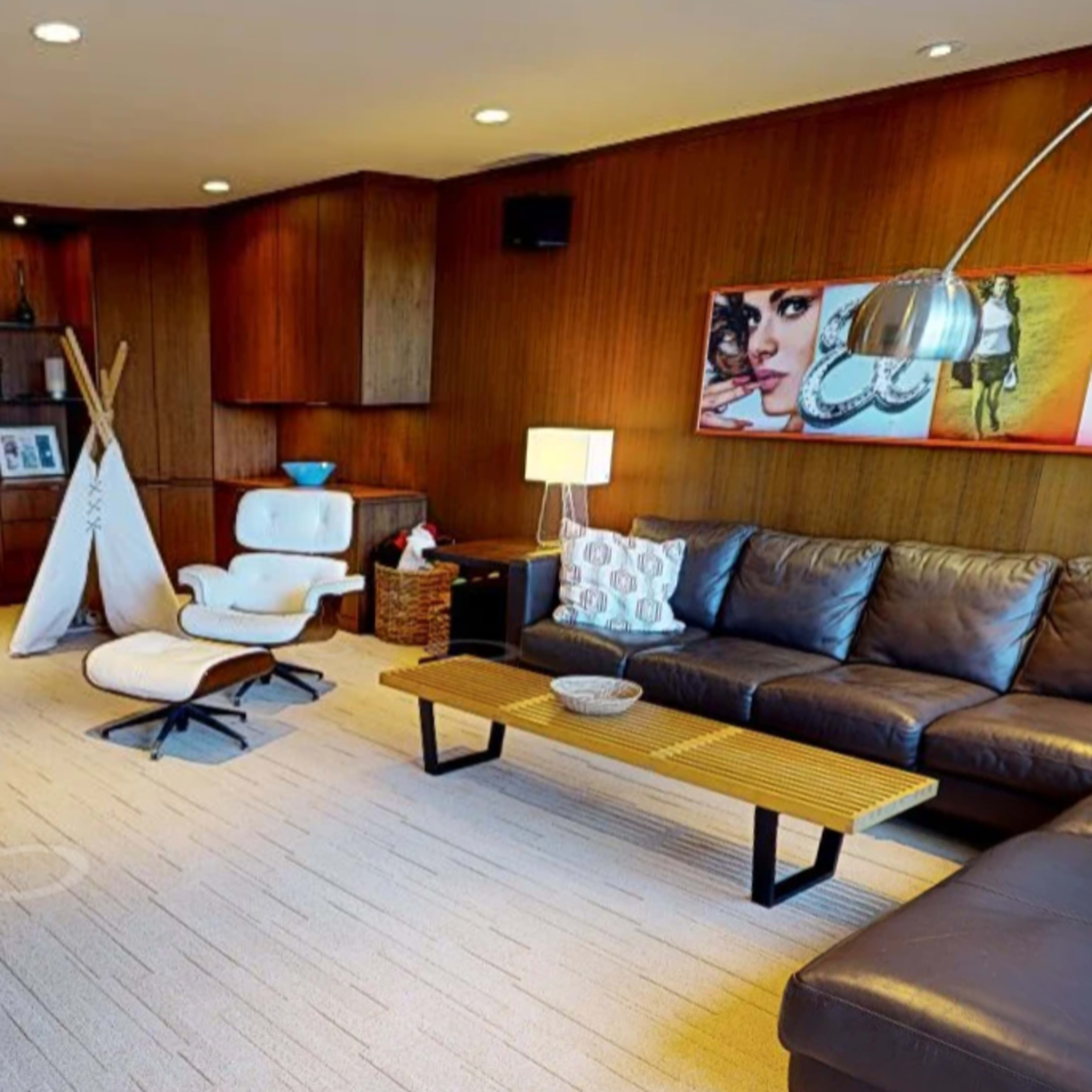 A modern living room featuring a sectional leather couch, a wooden coffee table, and framed artwork on the walls, with a stone accent behind the seating area.