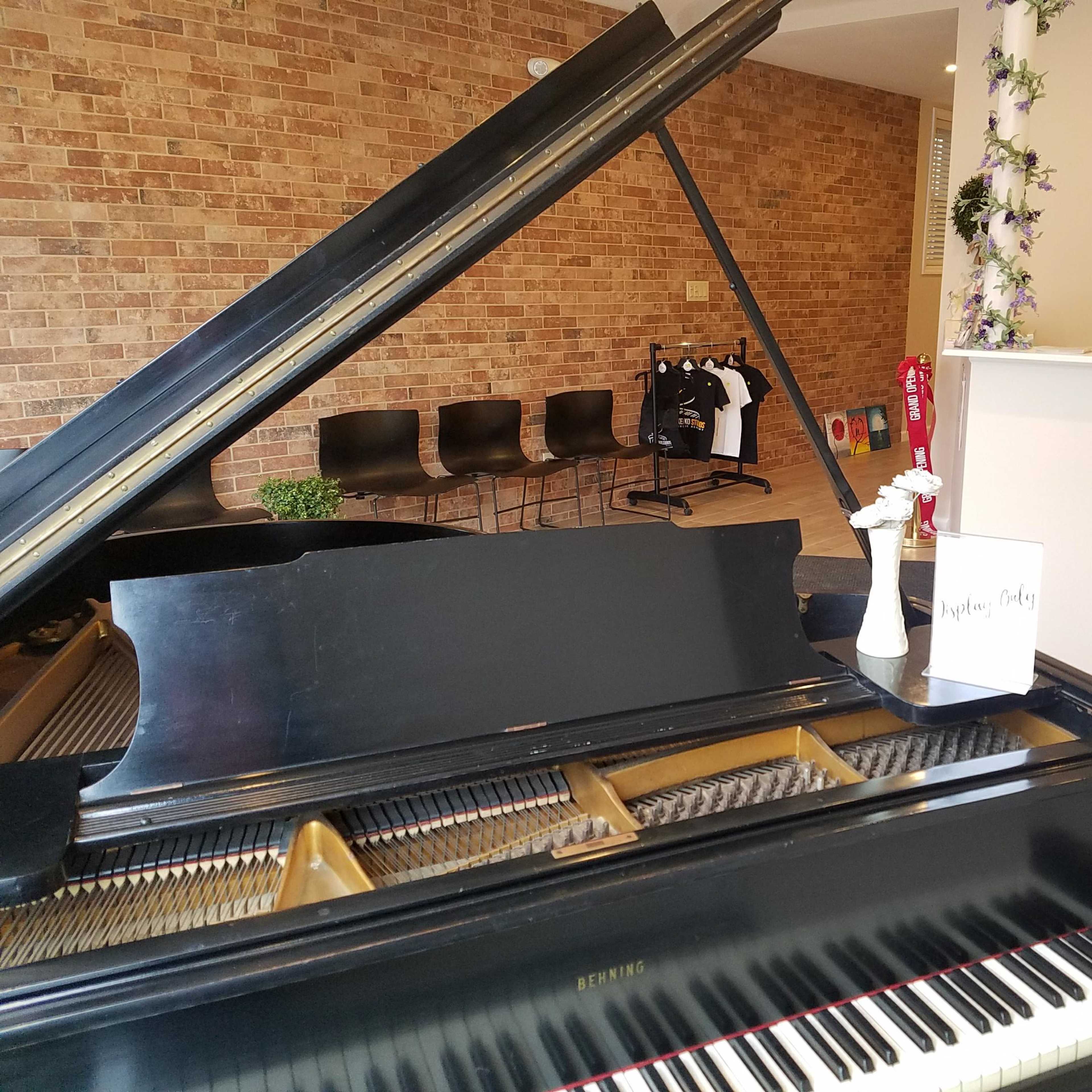 A grand piano positioned in a room with brick walls, accompanied by a white flower vase and a sign on a table.