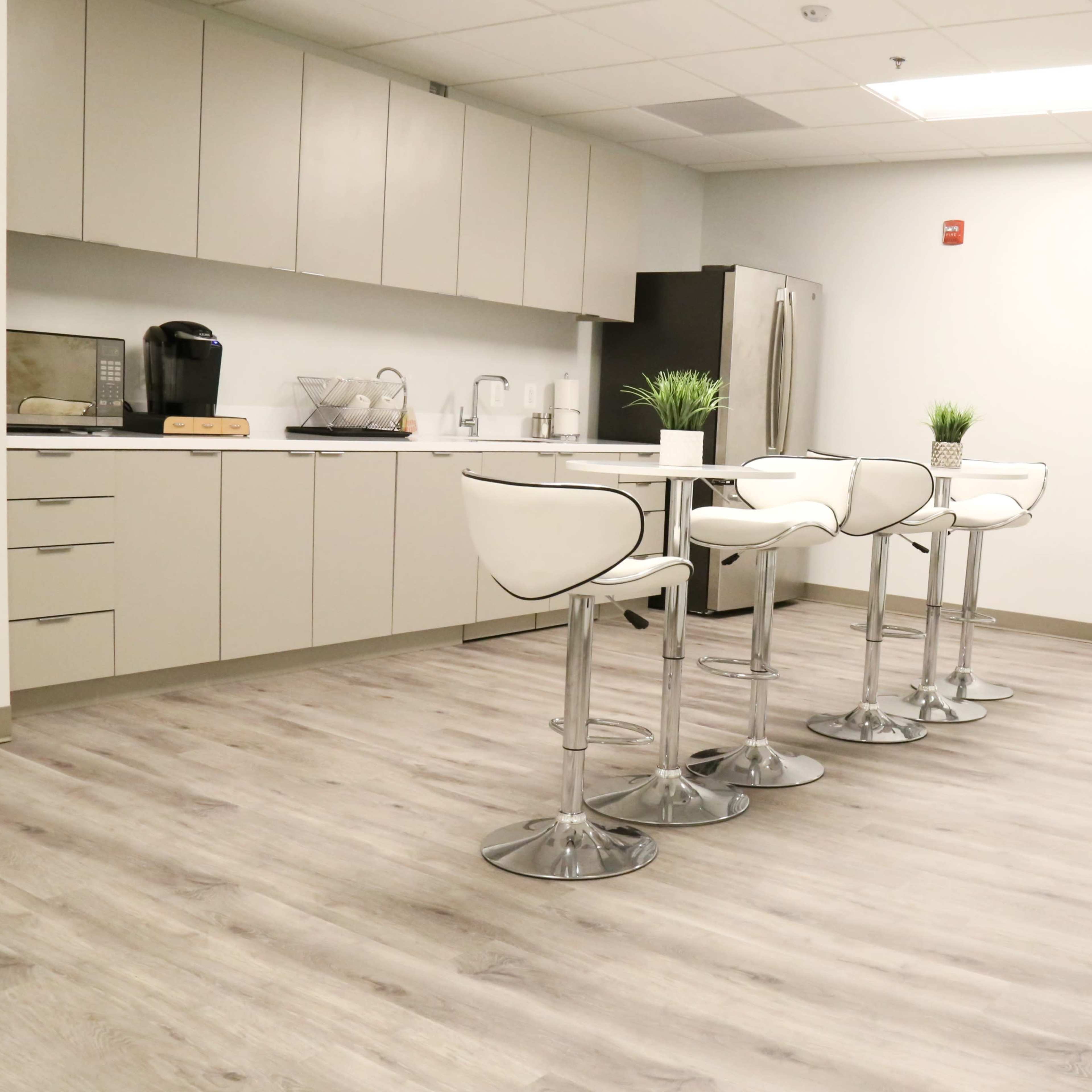 A modern kitchen area with a breakfast bar, four white stools, and stainless steel appliances.