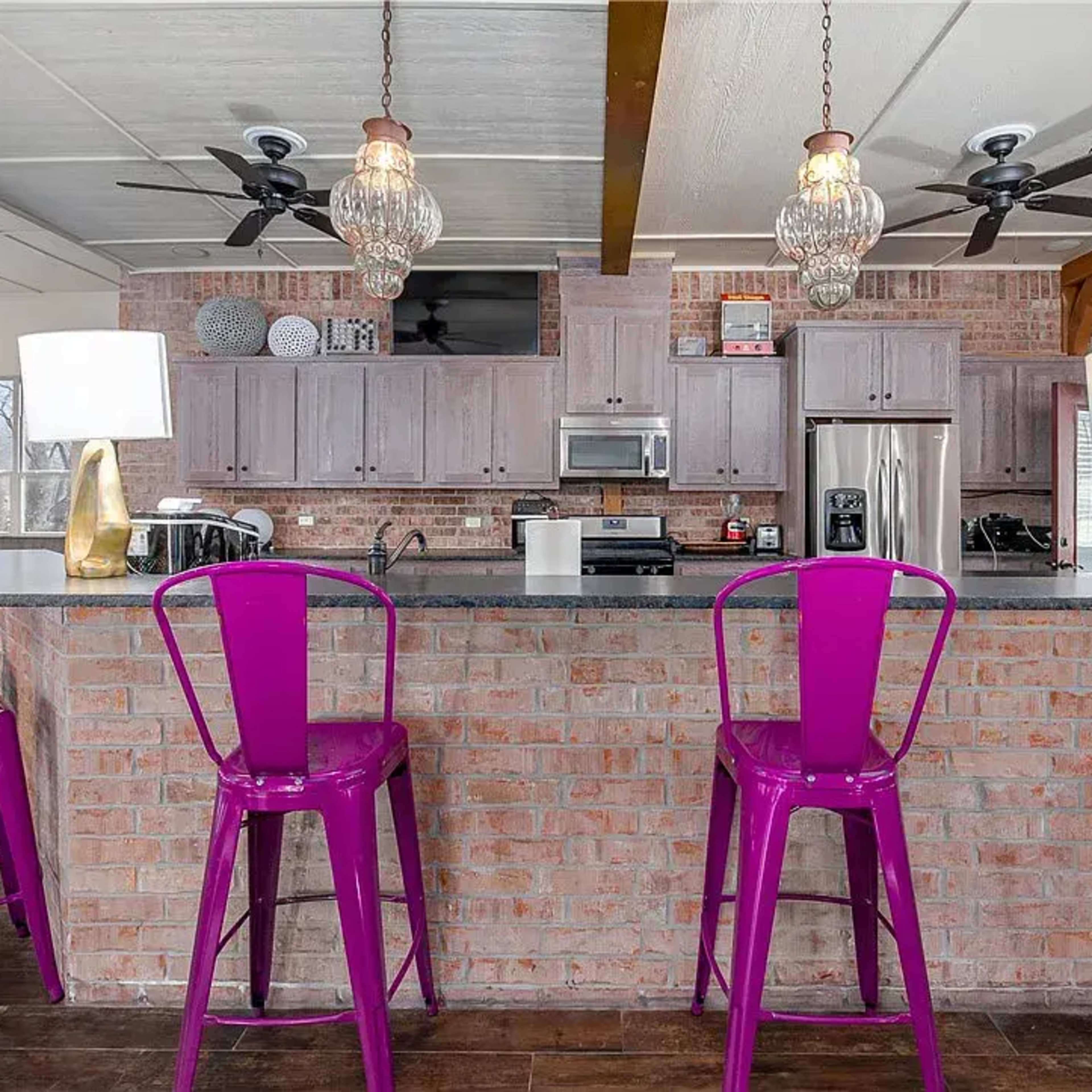 A modern kitchen with a brick island and four purple metal bar stools.