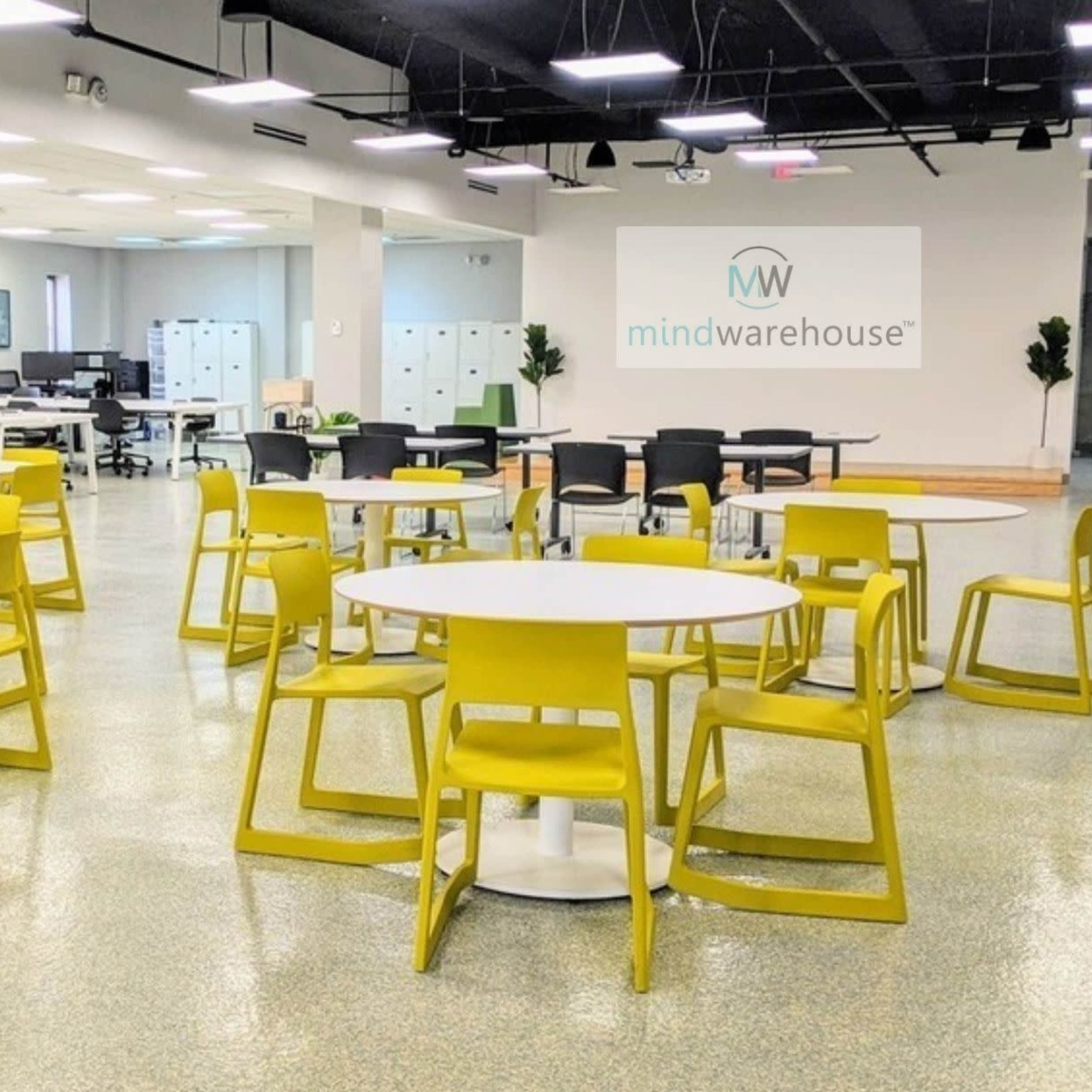 A spacious modern office area filled with several round tables and yellow chairs arranged for collaborative work.