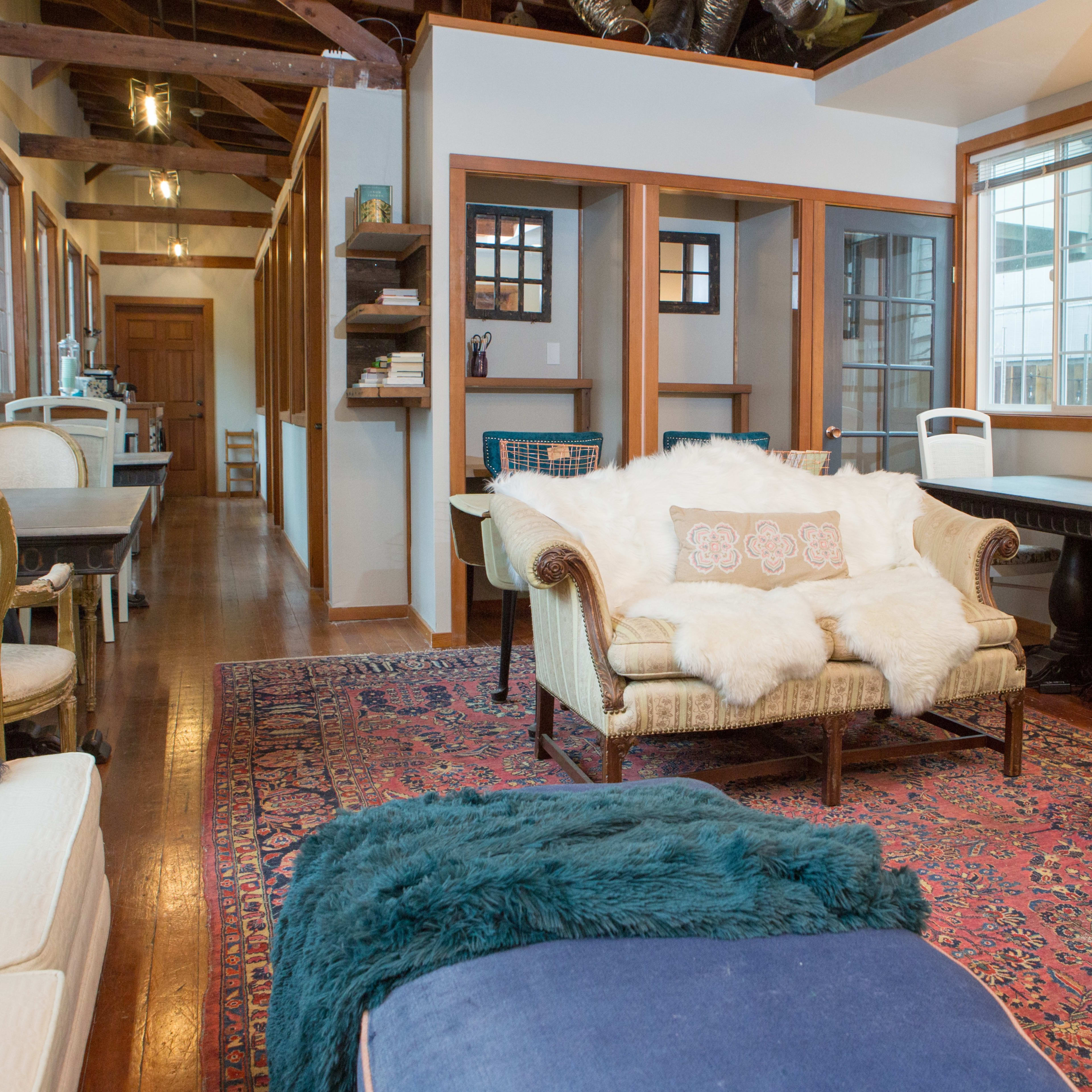 A cozy living space featuring a couch with a throw blanket, a coffee table, and a dining area in the background with wooden furniture and decorative elements.