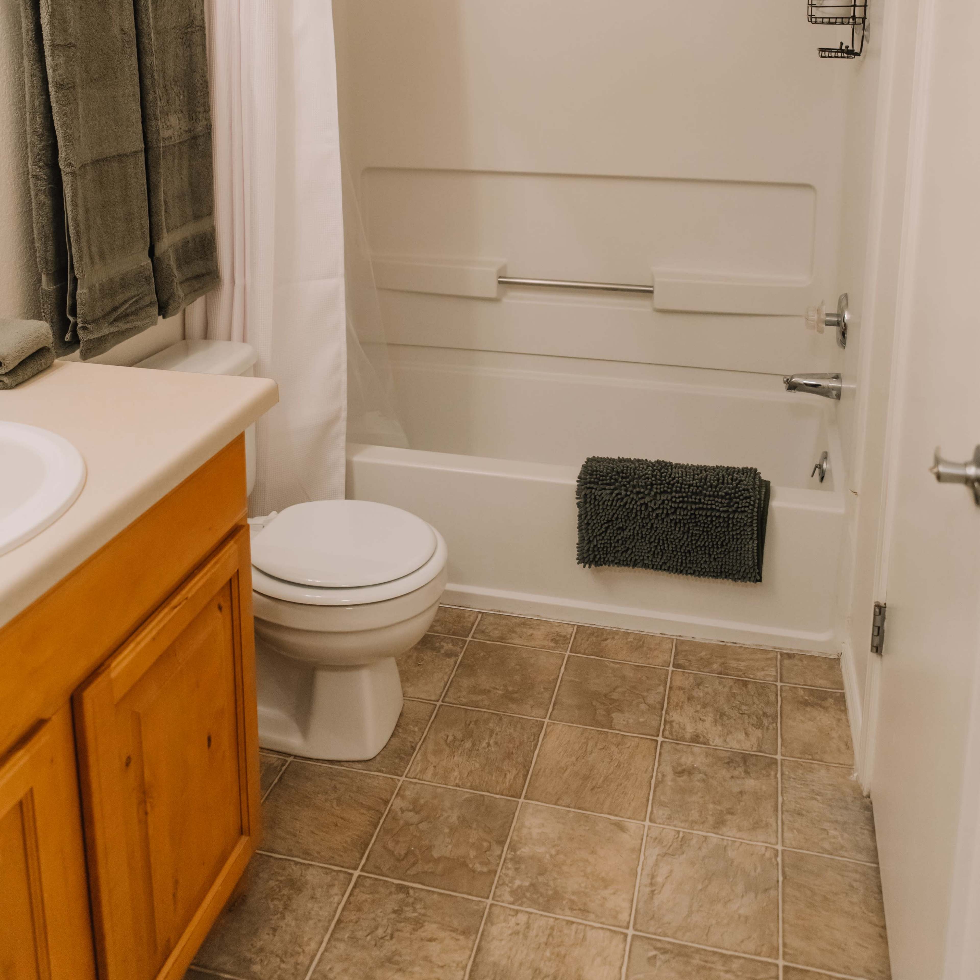 A small bathroom with a shower/tub combo, a toilet, a sink with a wooden cabinet, and neatly hung towels.