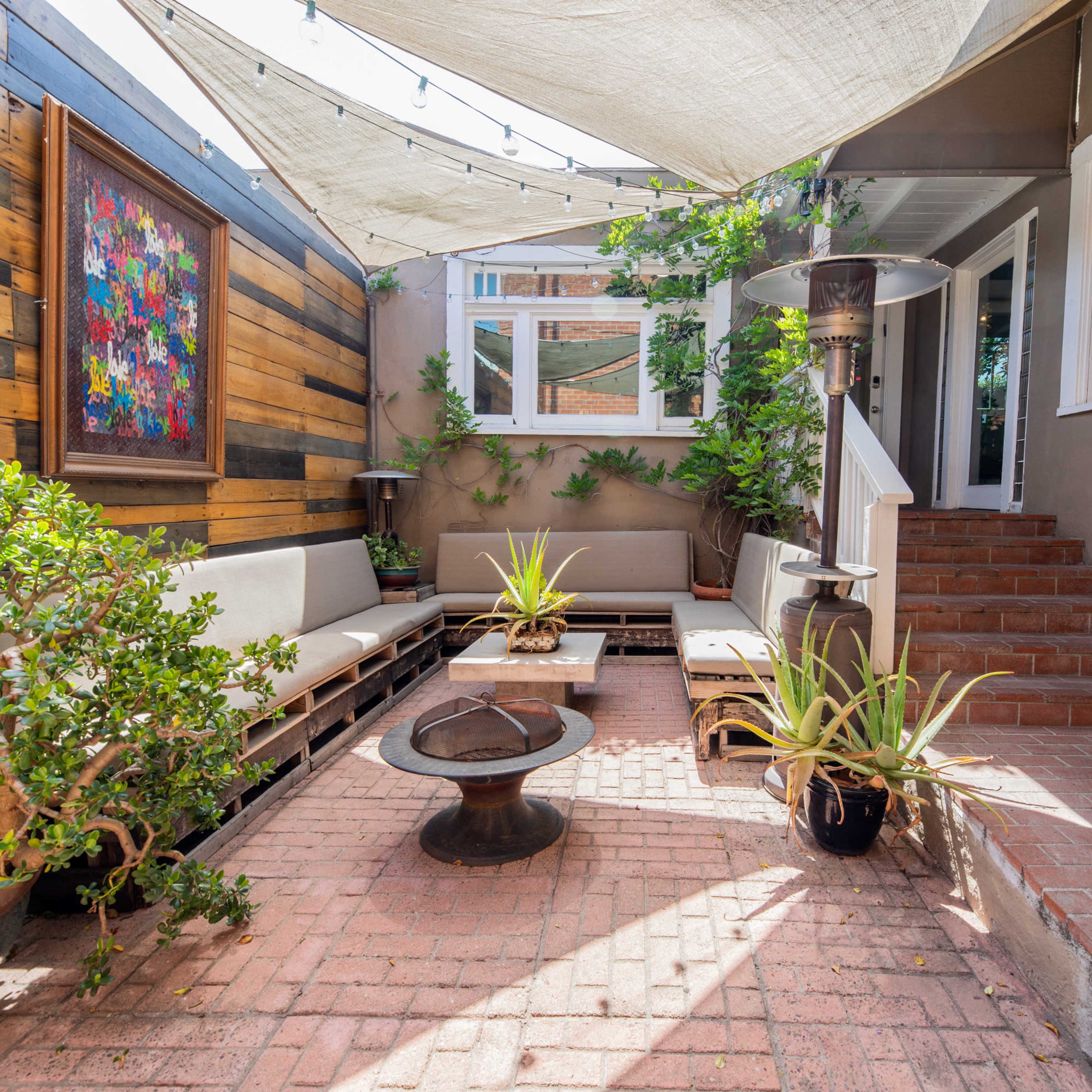 A patio area featuring a covered seating arrangement, a fire pit, potted plants, and steps leading to an interior space.