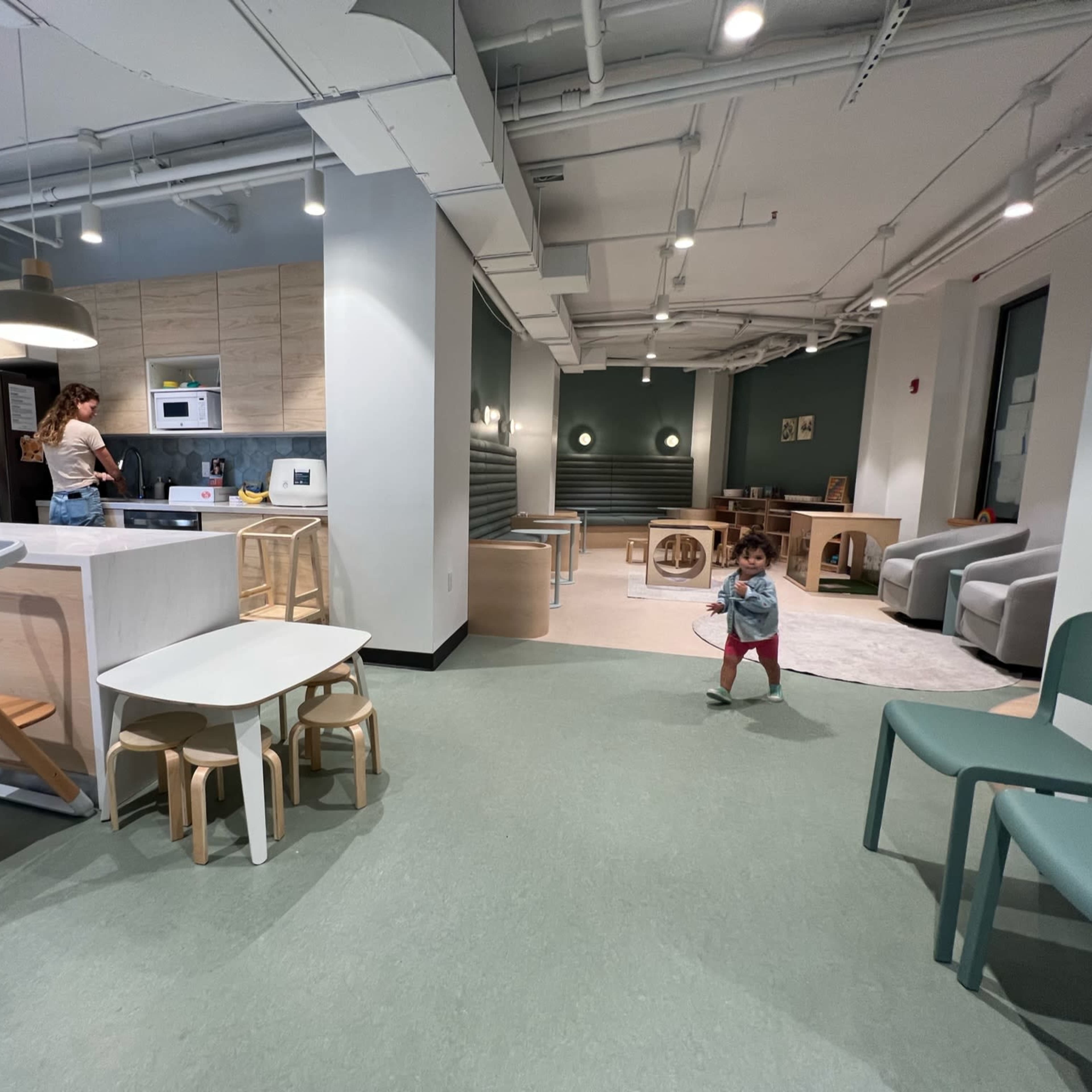 A spacious indoor play area features a kitchen, seating, and a child playing on the floor.