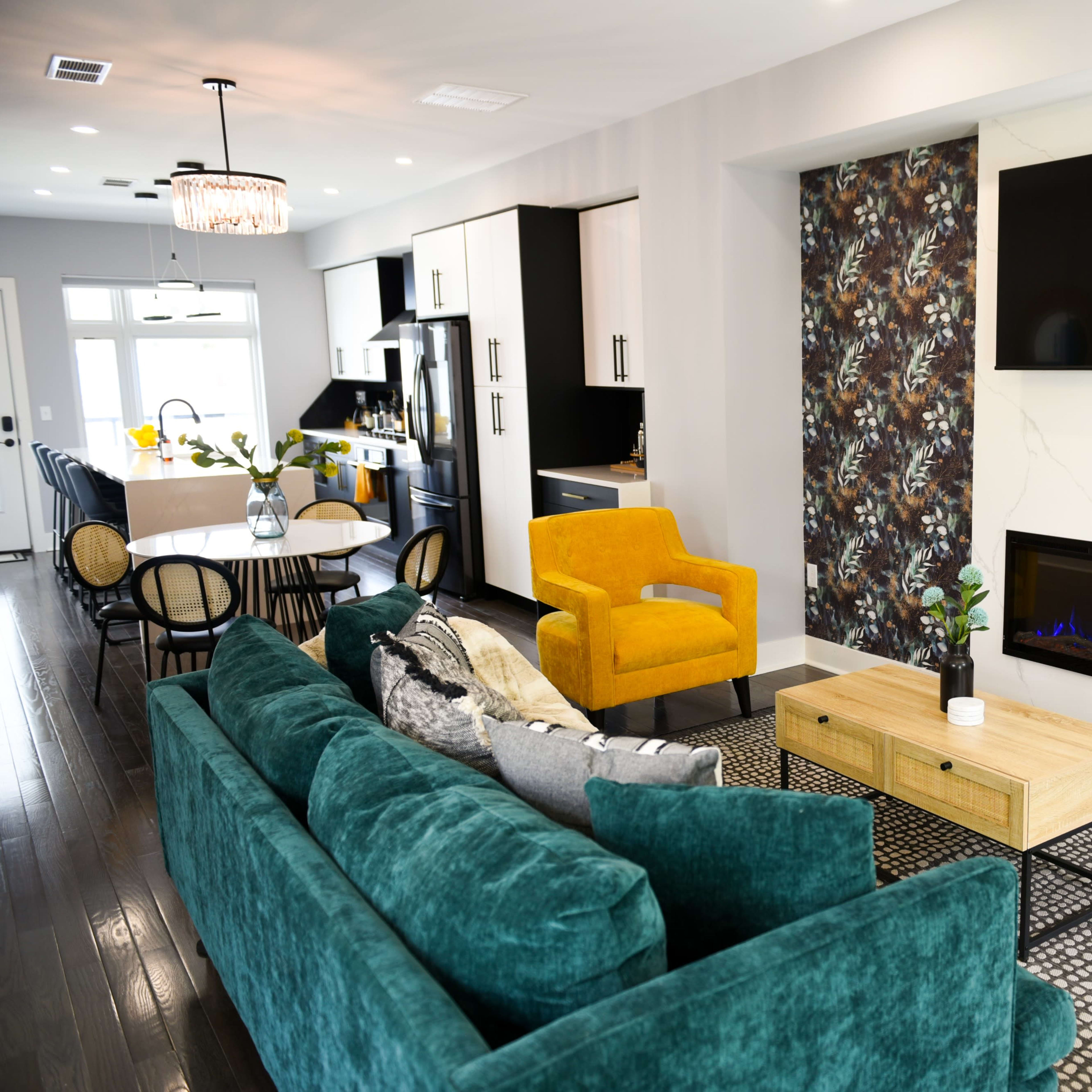 A modern living room featuring a teal sofa, yellow armchairs, a wooden coffee table, and a wall-mounted TV above a fireplace.