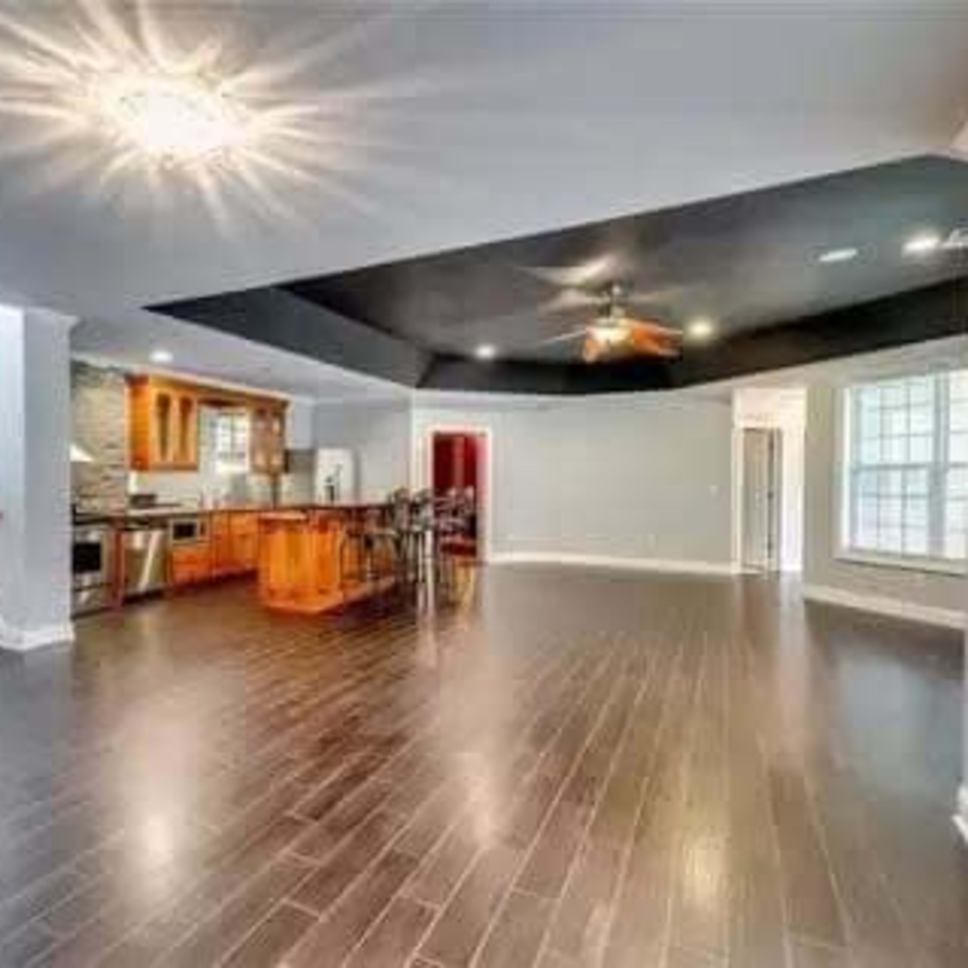 A spacious interior living area with dark wood flooring, a kitchen in the background, and a staircase leading to another level.