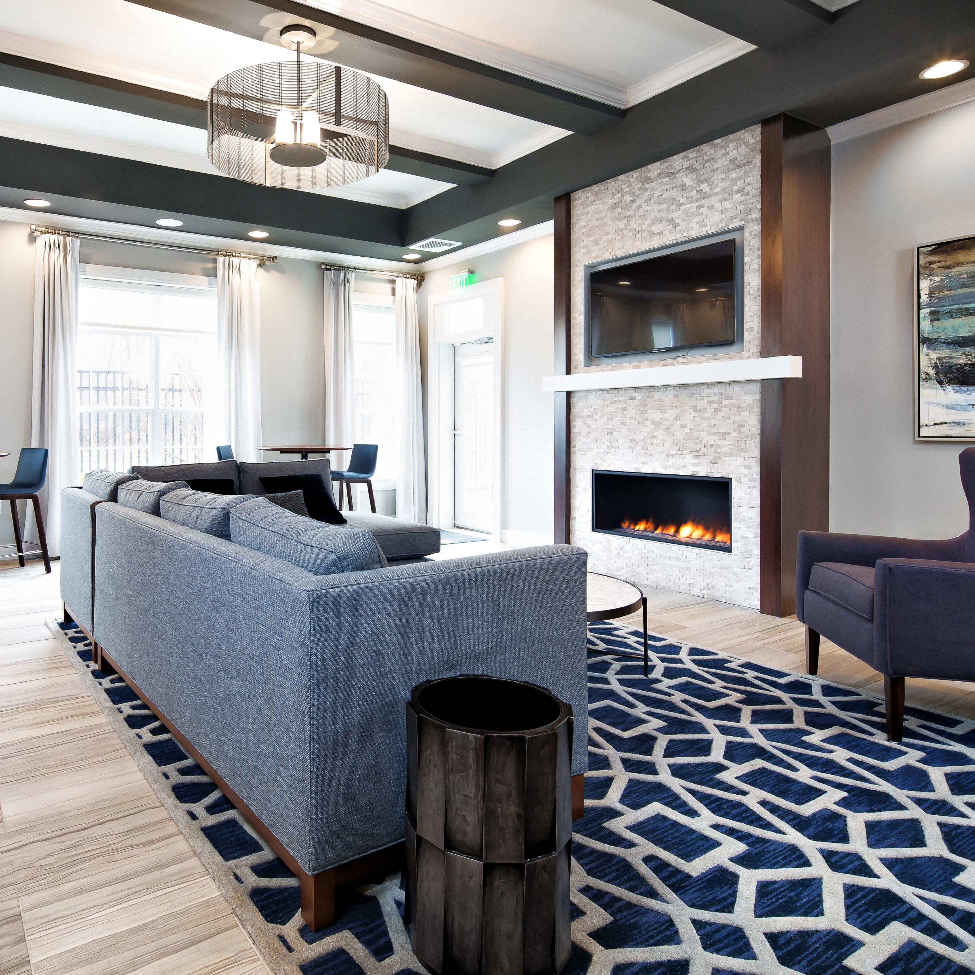 A modern lounge area features a blue sofa, a stone fireplace, and large windows allowing natural light to fill the space.