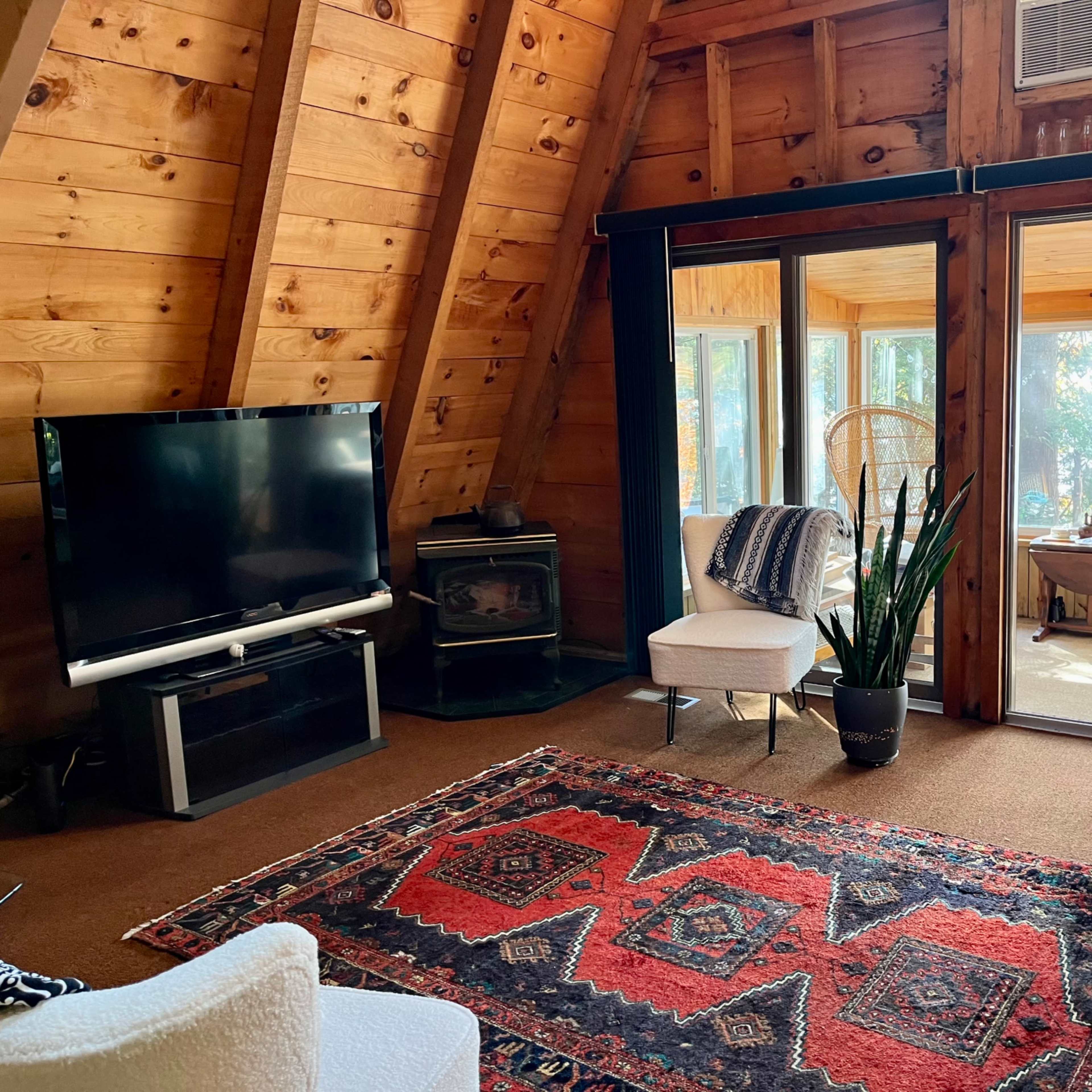 A wood-paneled living room with a television, a fireplace, and large windows overlooking a sunroom.