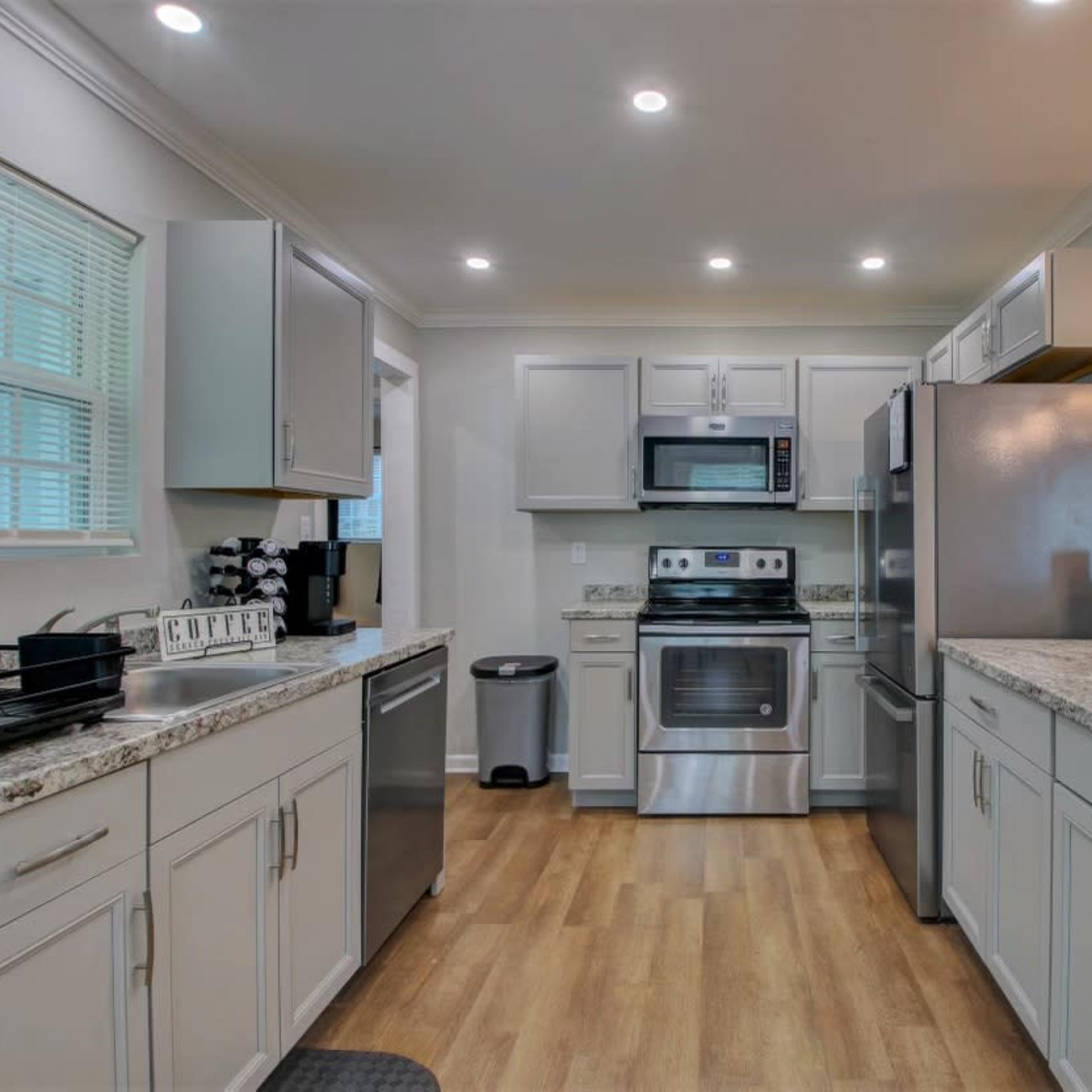 The kitchen features light gray cabinetry, stainless steel appliances, and a granite countertop with wooden flooring.