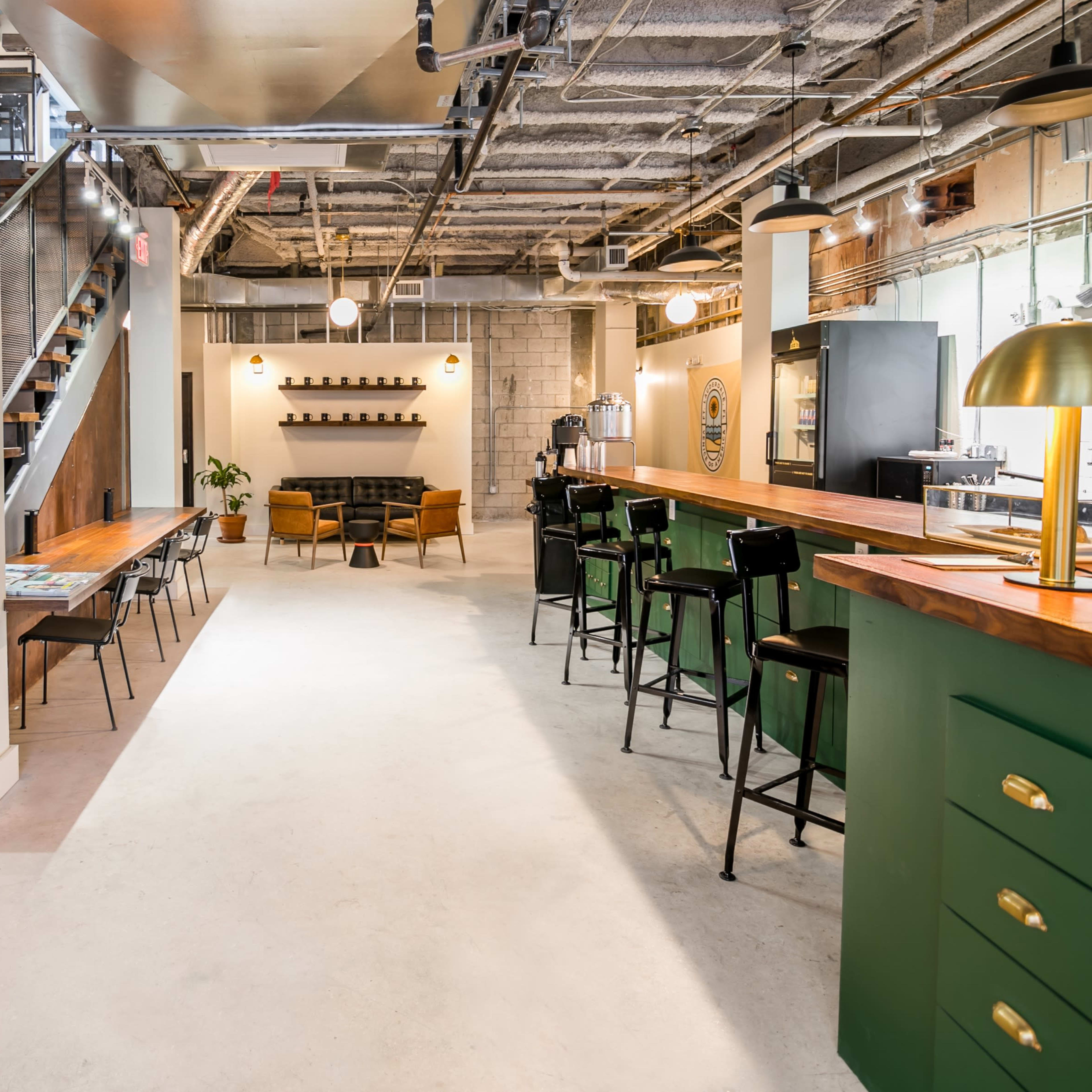 A modern interior space featuring a staircase, a wooden bar with green accents, seating areas, and a minimalist design.