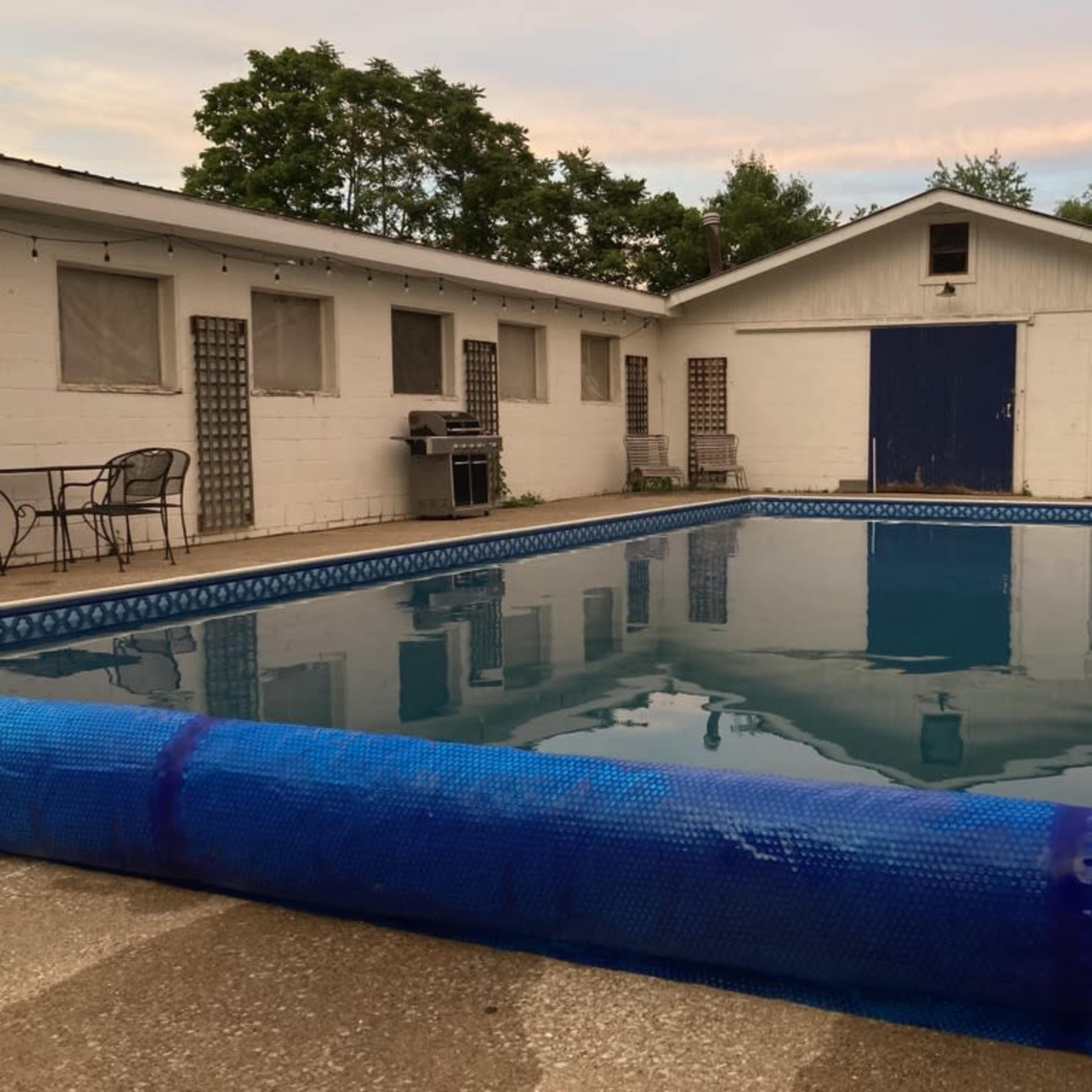 A rectangular swimming pool is surrounded by a concrete patio and a white building with blue doors and windows.