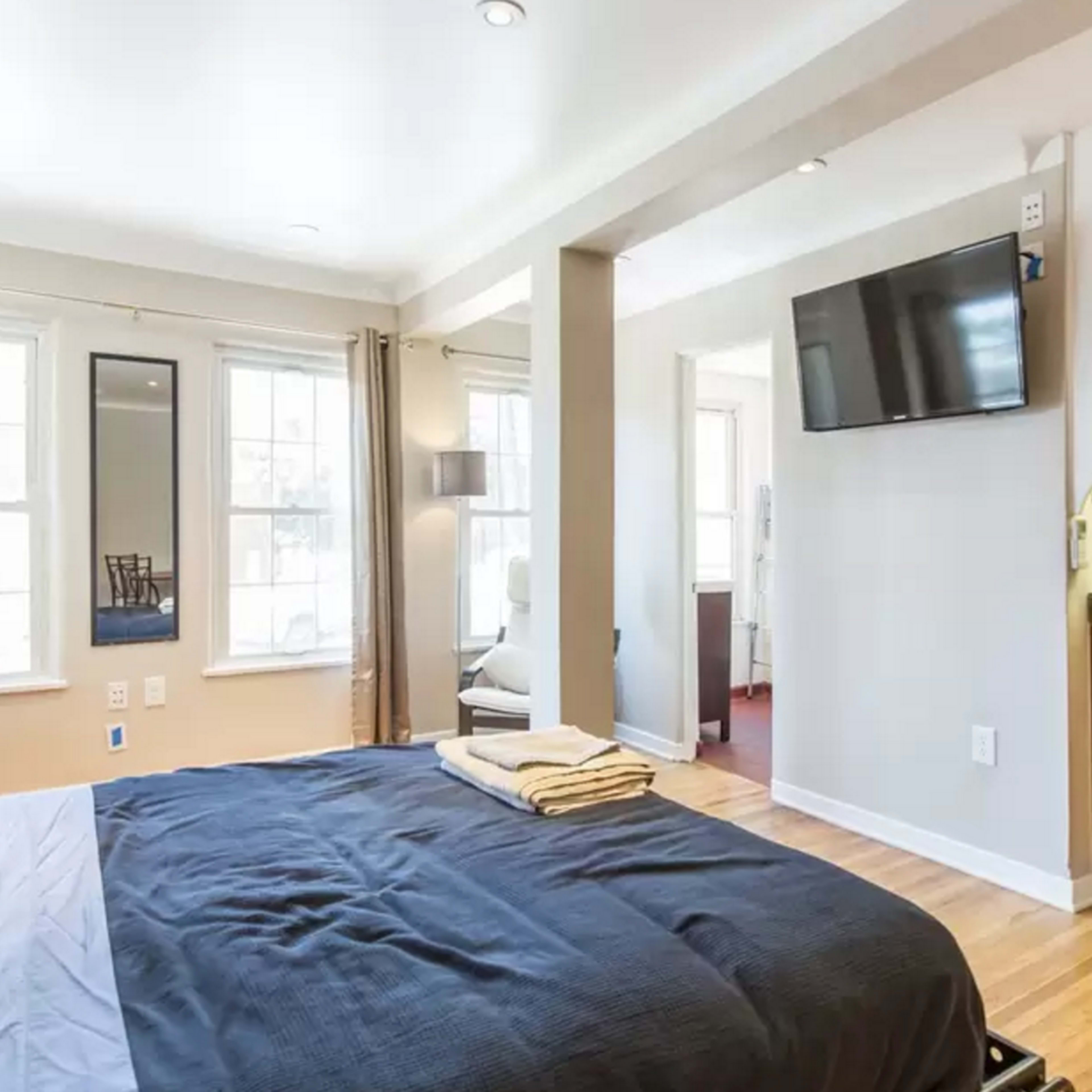 A bedroom with a bed, a television mounted on the wall, and a small kitchenette area.