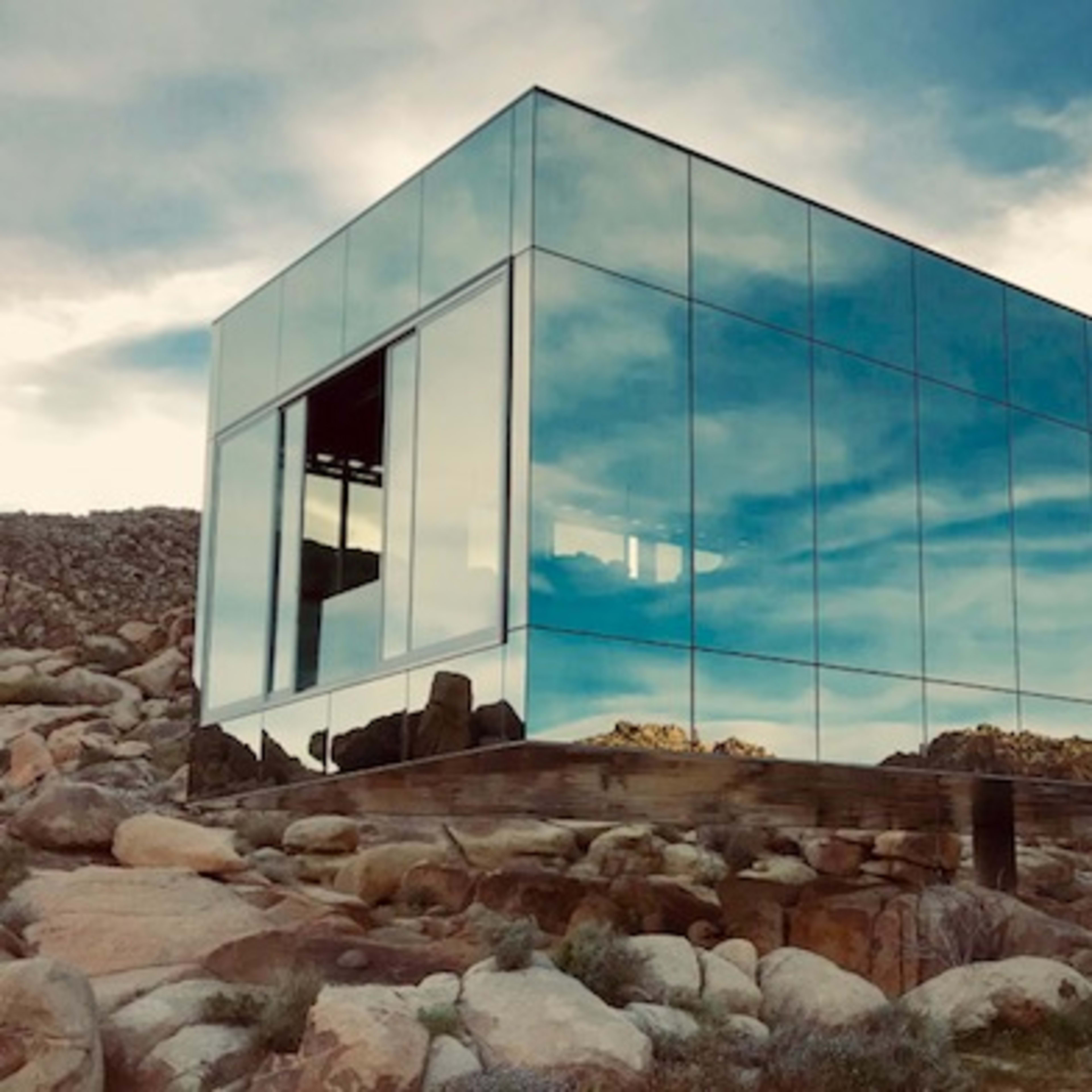 A modern glass building reflecting the surrounding rocky landscape under a cloudy sky.