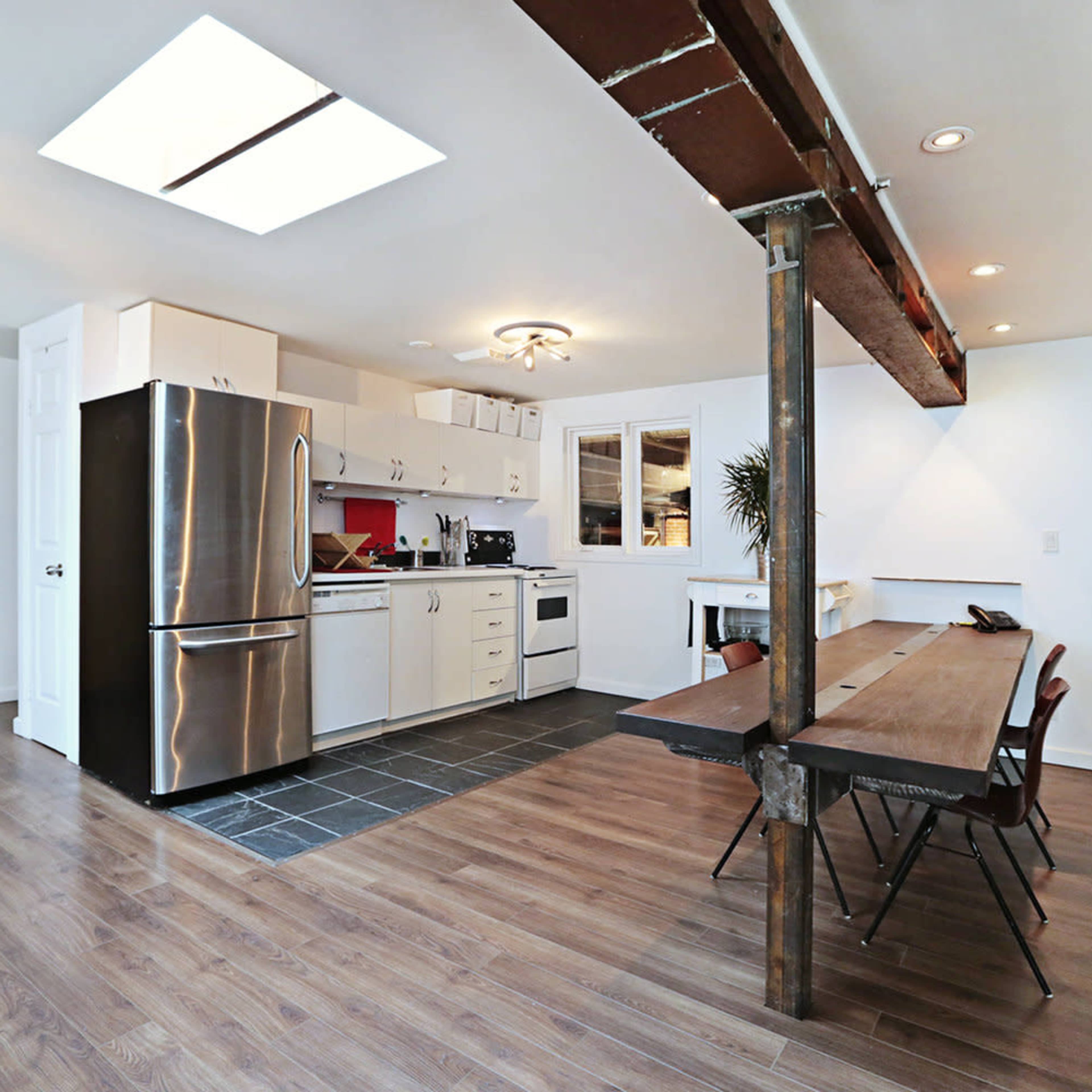 A modern kitchen and dining area featuring stainless steel appliances, a wooden dining table, and a sliding door leading to another room.