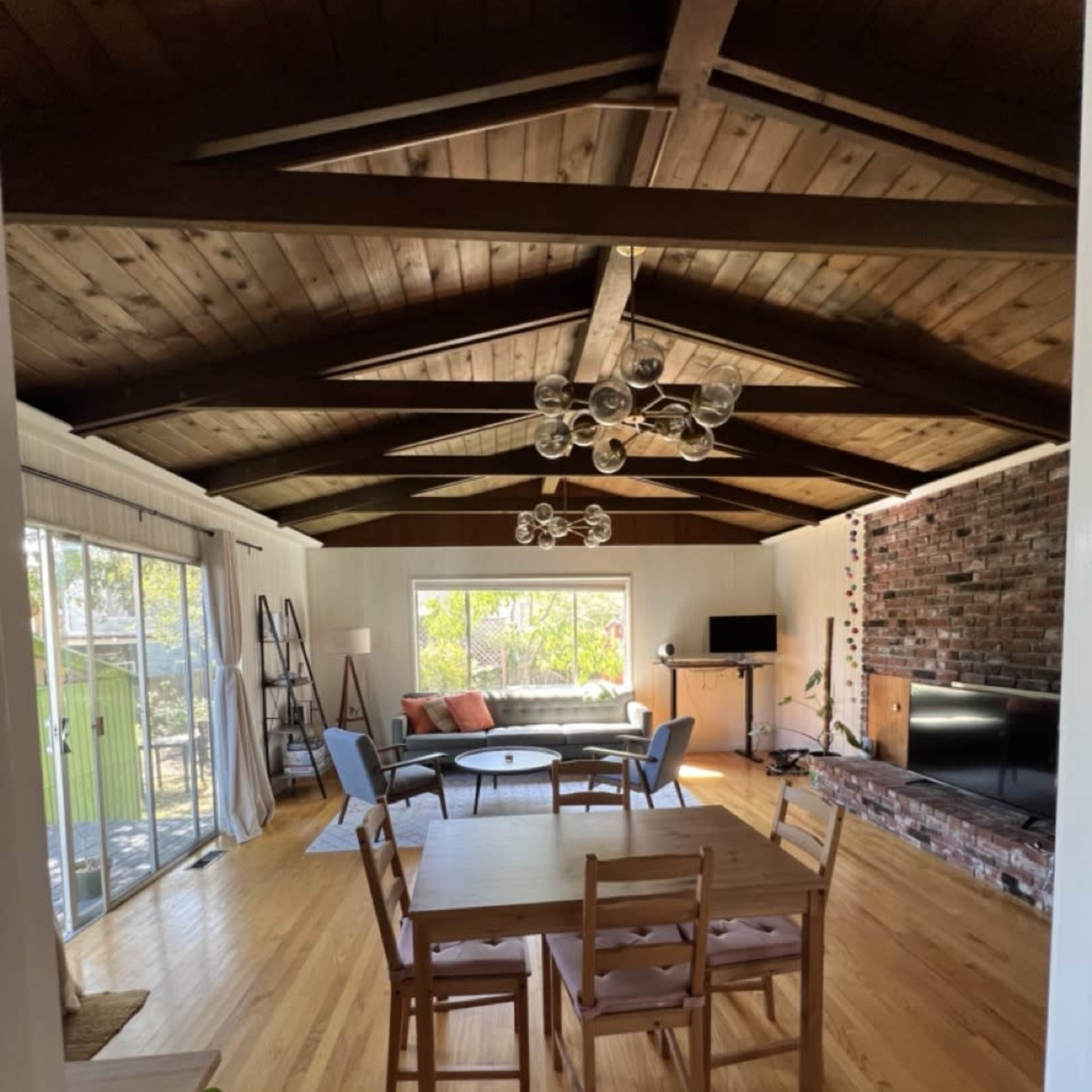 A spacious living room features a wooden ceiling, large windows, and a seating area with a couch and chairs.
