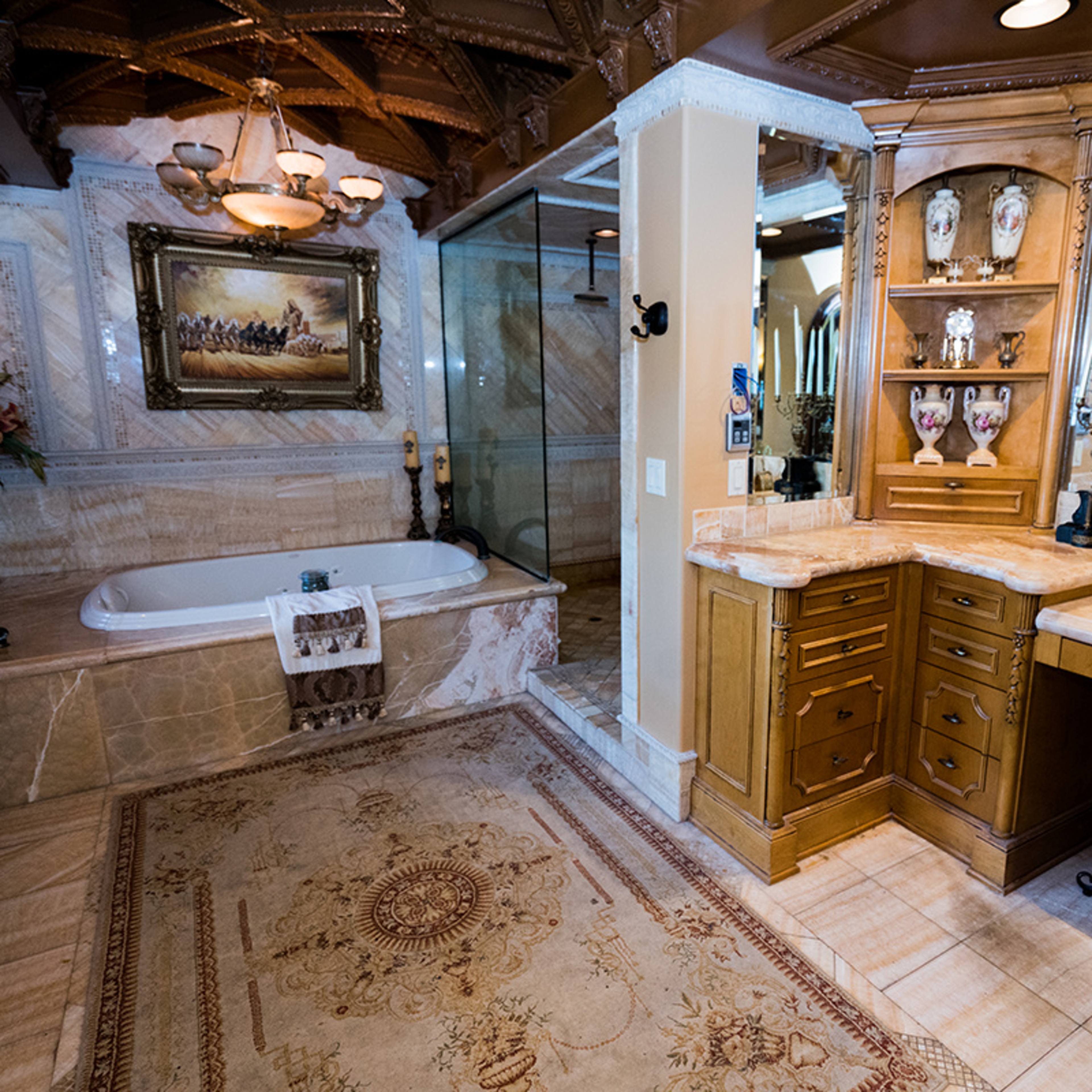A luxurious bathroom featuring a large bathtub, a glass shower, wooden cabinetry, and ornate decor, all set against marble walls and flooring.