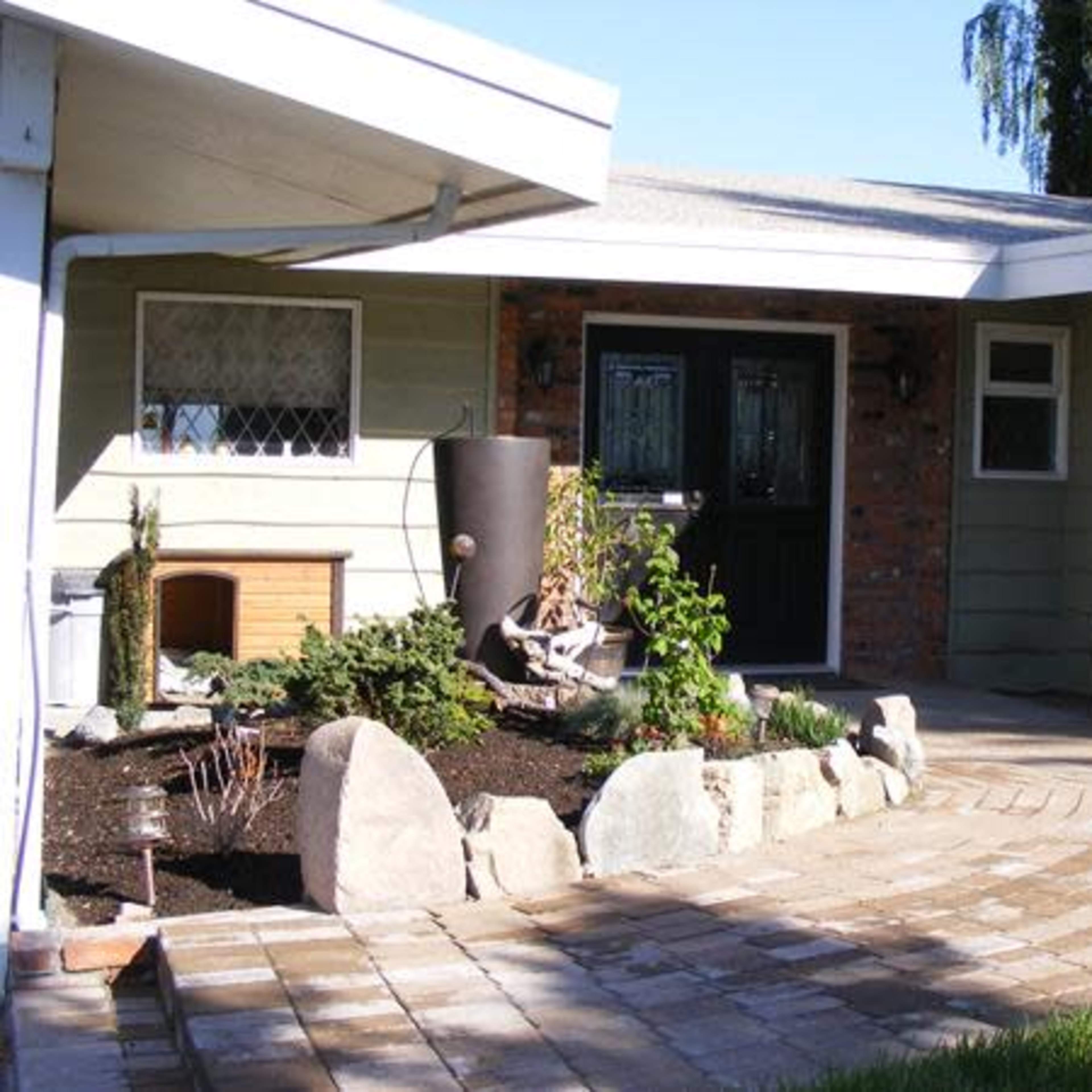 A landscaped patio area with a curved stone pathway leading to a green front door and a garden featuring plants and decorative stones.