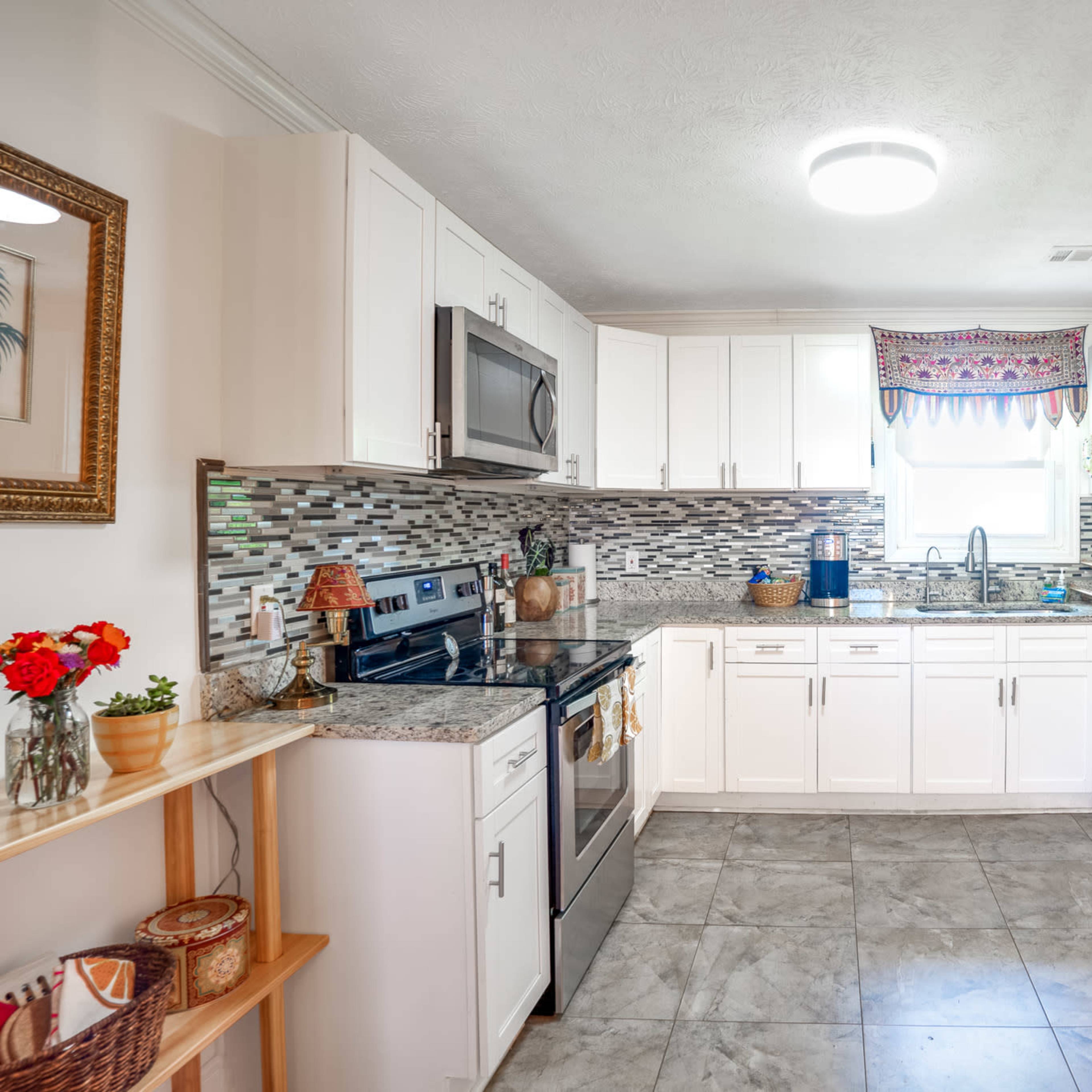 A modern kitchen features white cabinets, stainless steel appliances, and a tiled backsplash with a breakfast nook on the side.