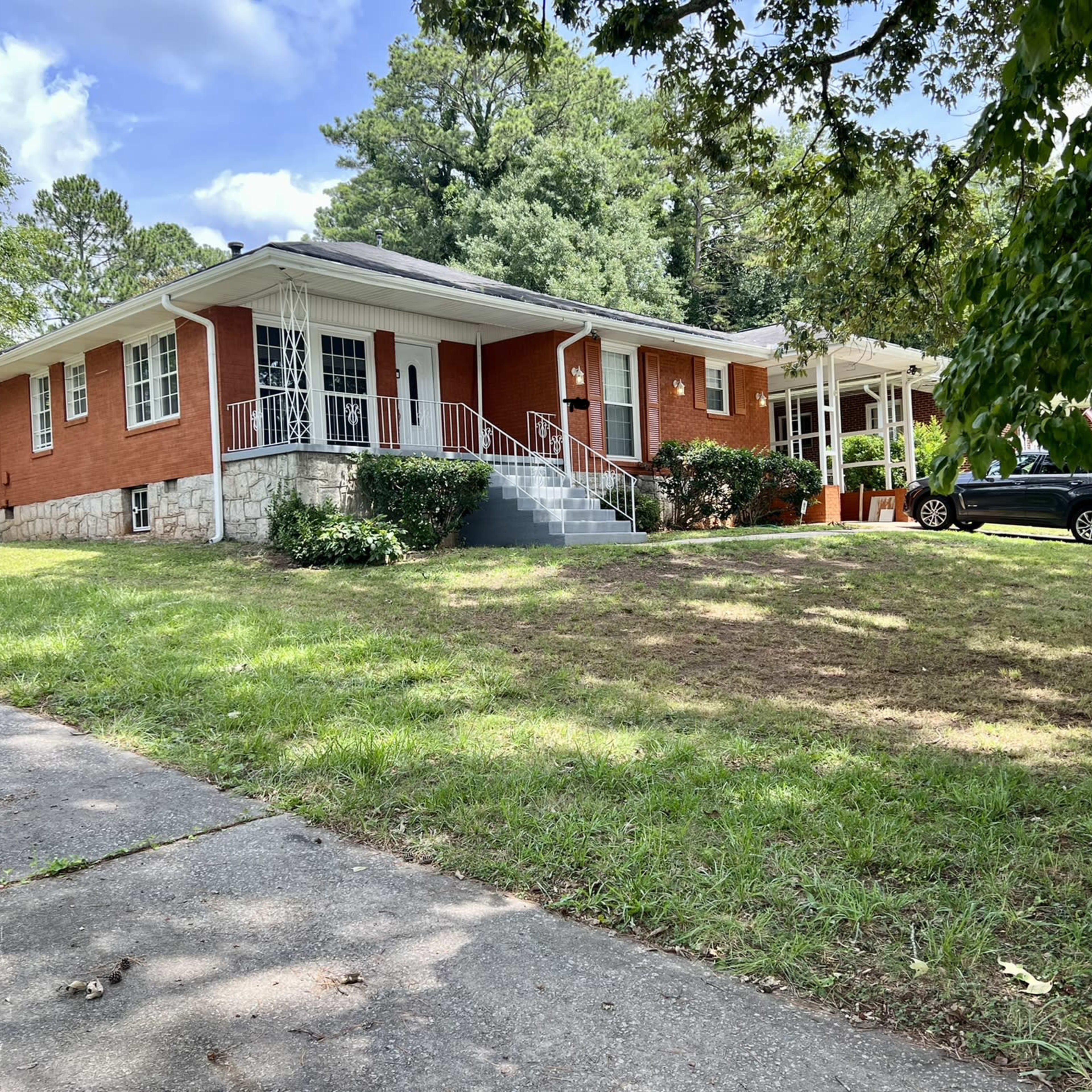 A brick house with a stone foundation is set back from the street, surrounded by a grassy lawn and trees.