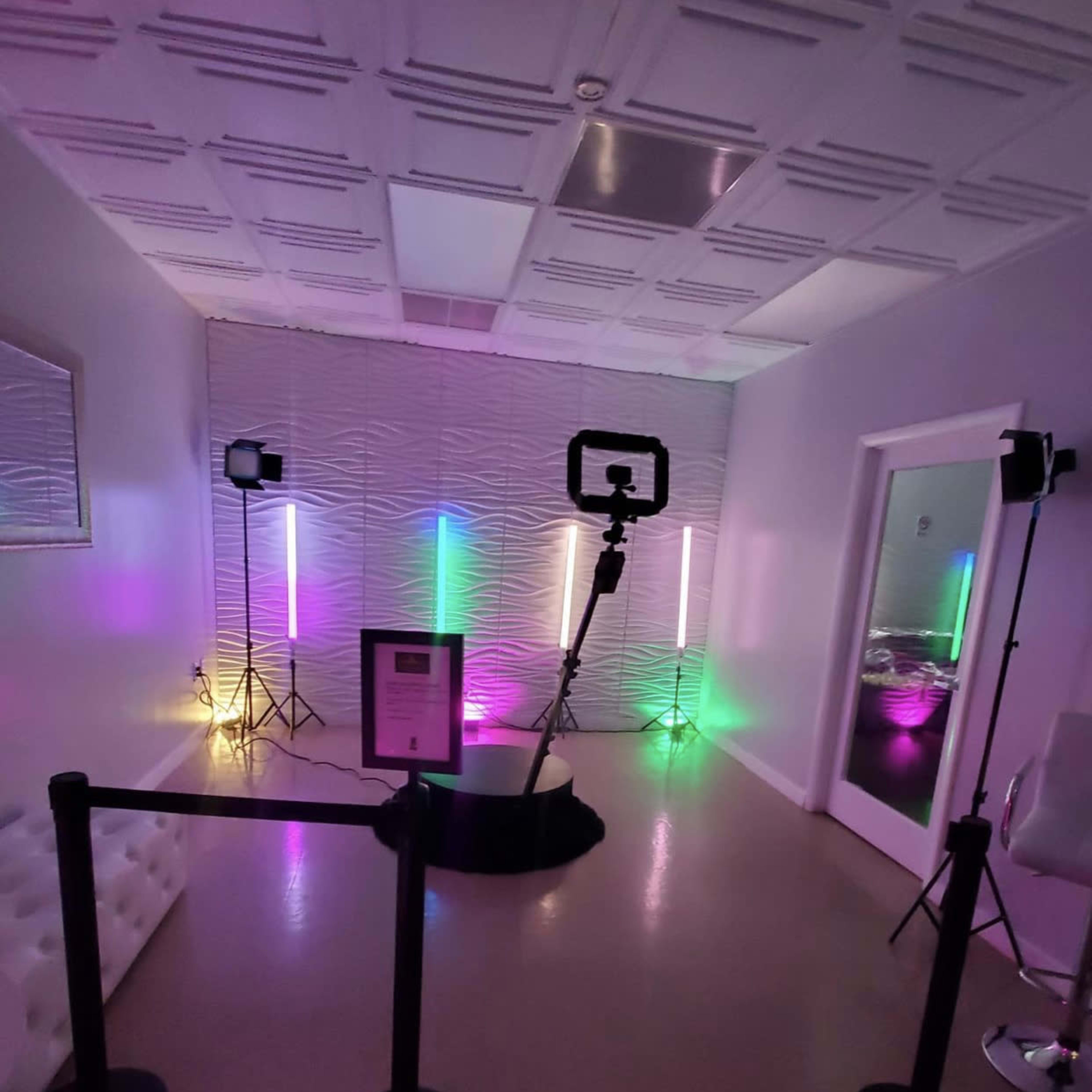 A modern room with colorful lights, a tripod with a ring light, and a velvet rope barrier separating the setup from the rest of the space.