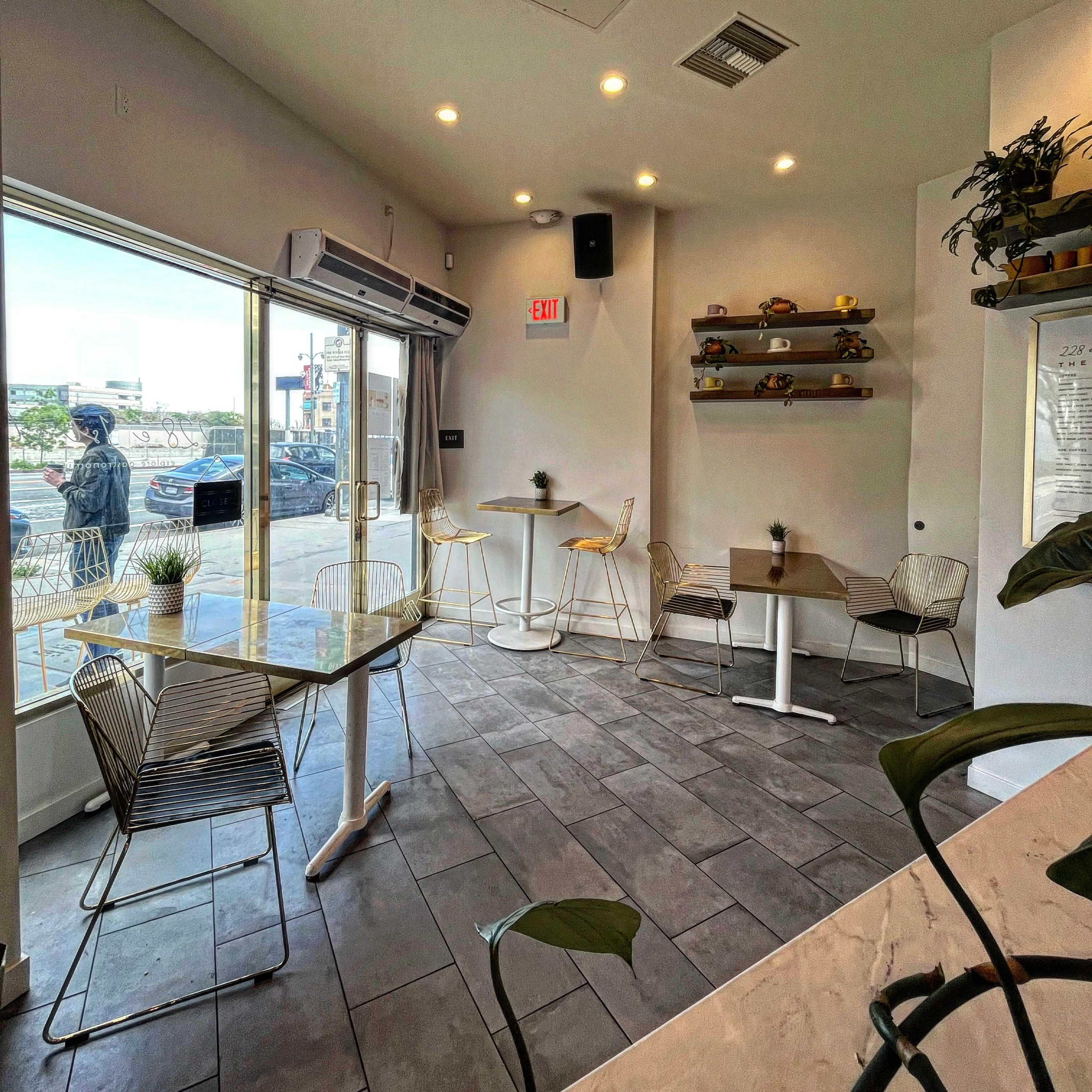 A modern café interior with a glass table, metal chairs, and shelves displaying decorative items, illuminated by recessed lighting.