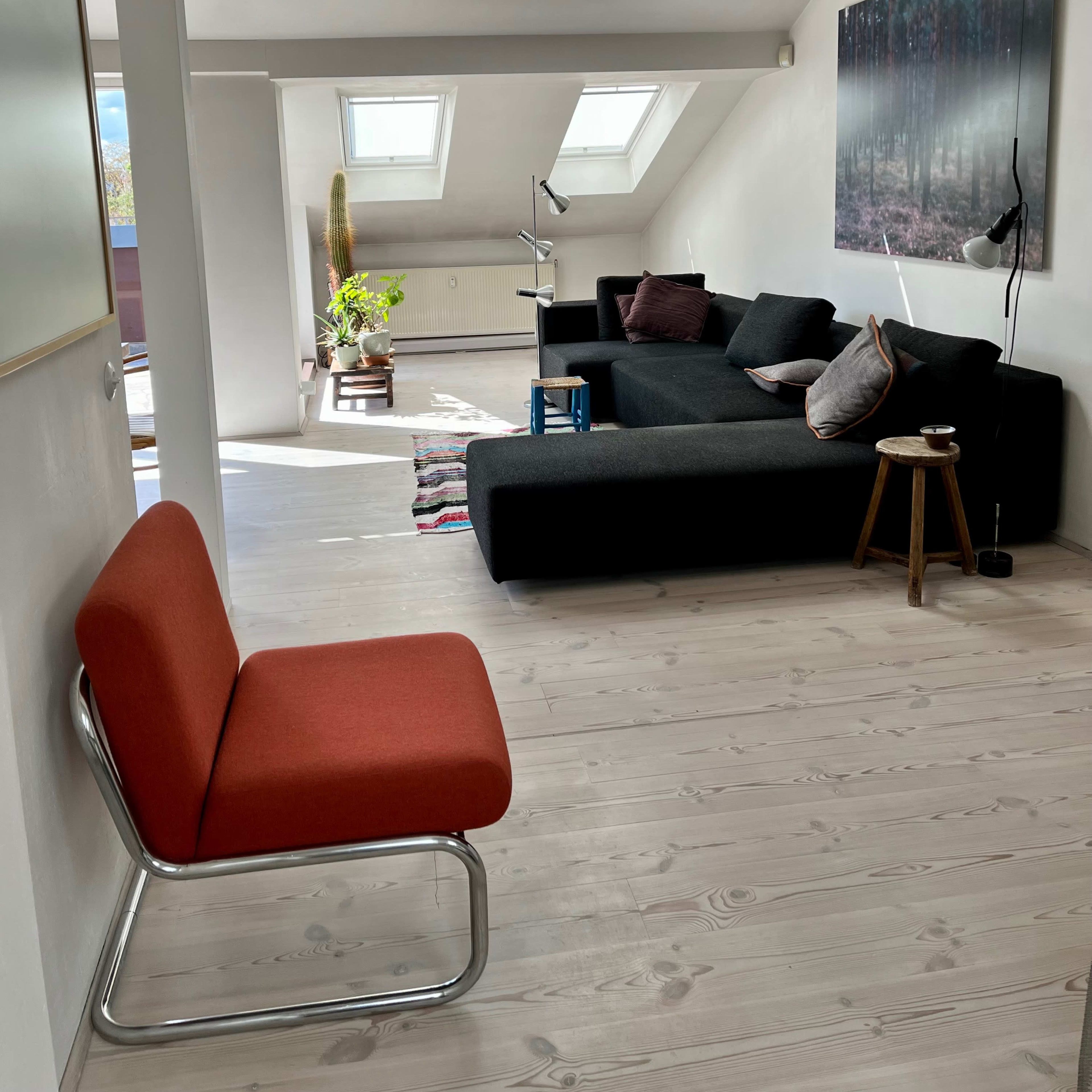 A modern, airy living room with a black sectional sofa, a wooden floor, and skylights illuminating the space.