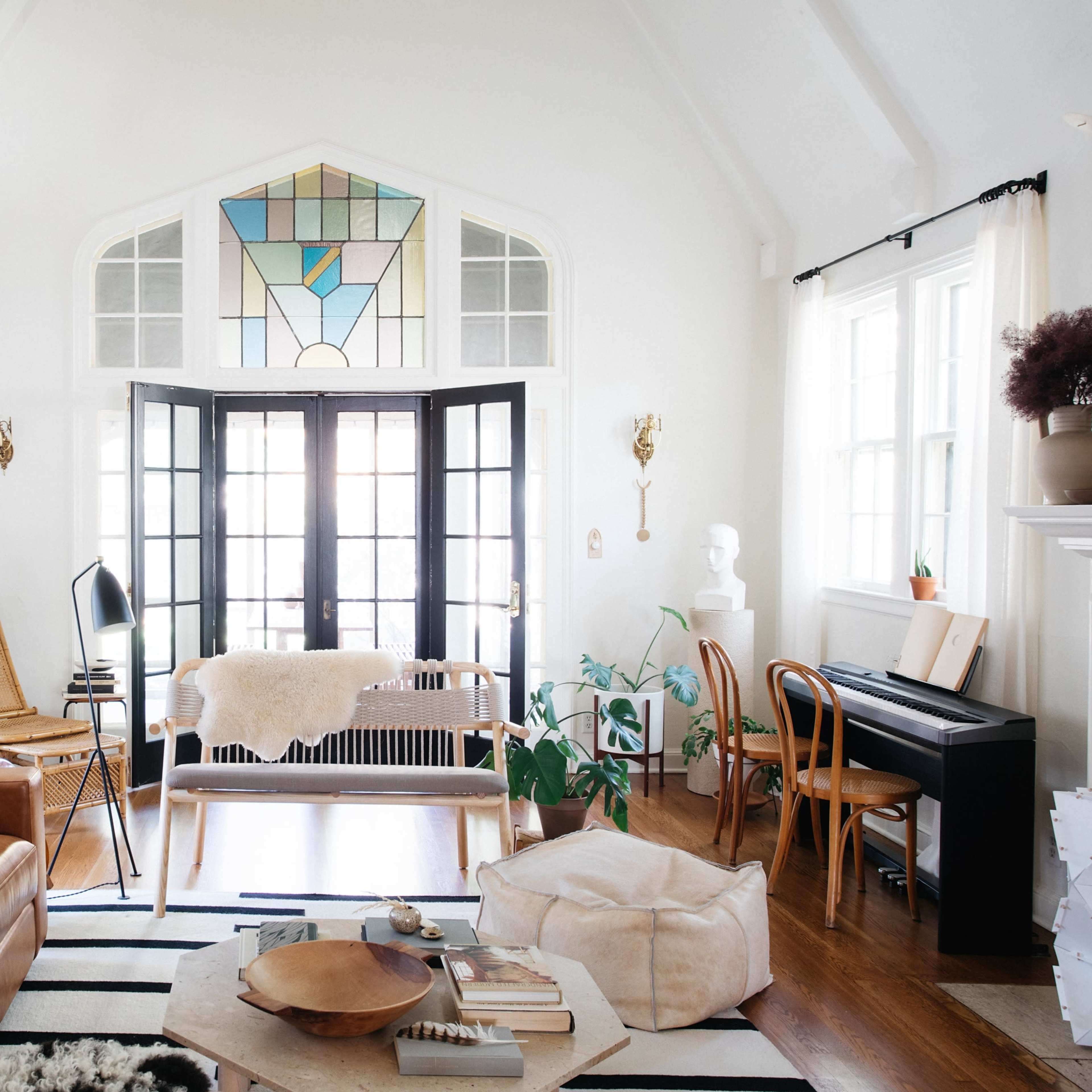 A bright living room with large windows, a mix of comfortable seating, indoor plants, and a stylish decorative stained glass window.