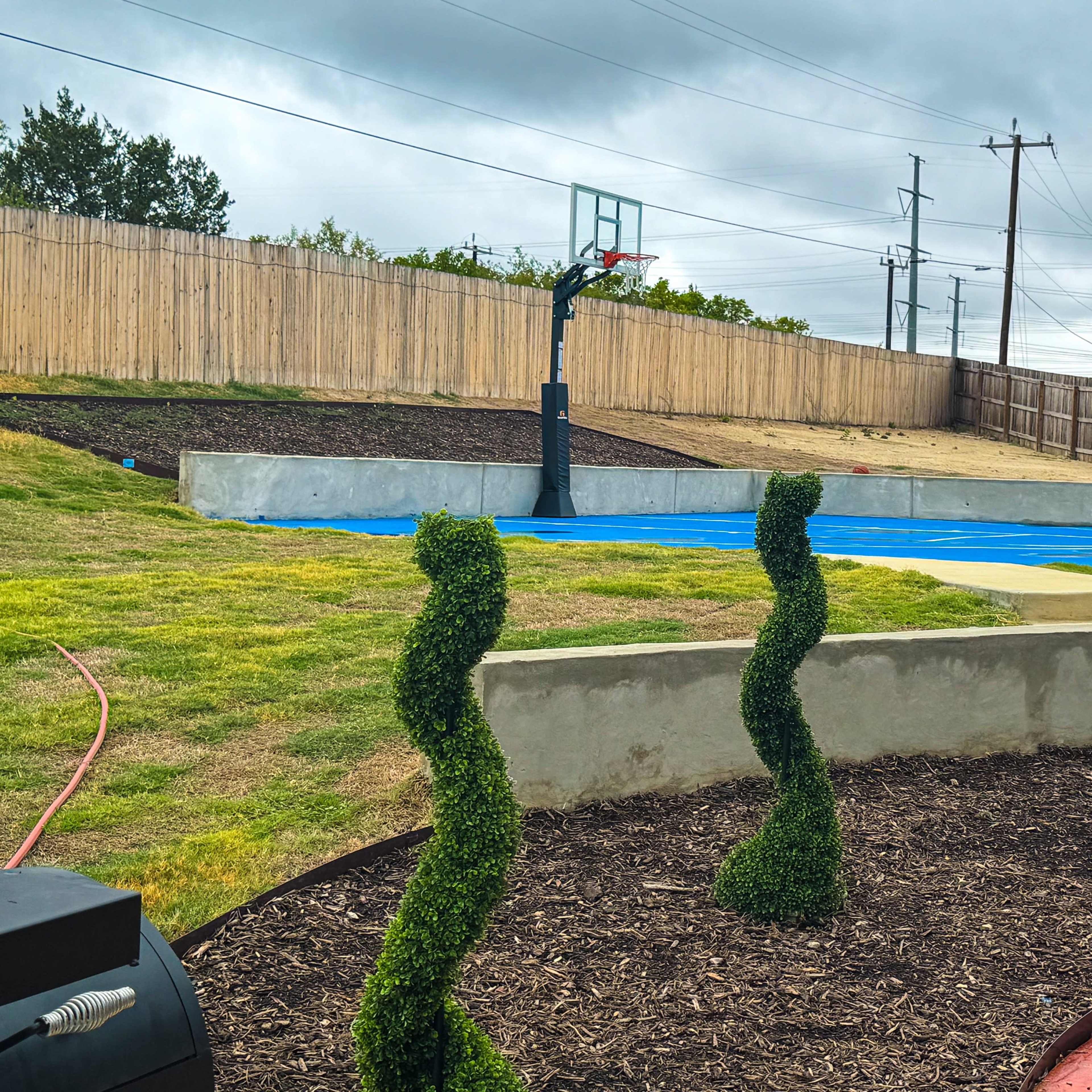 A basketball court surrounded by a grassy area with three topiary sculptures in the foreground.