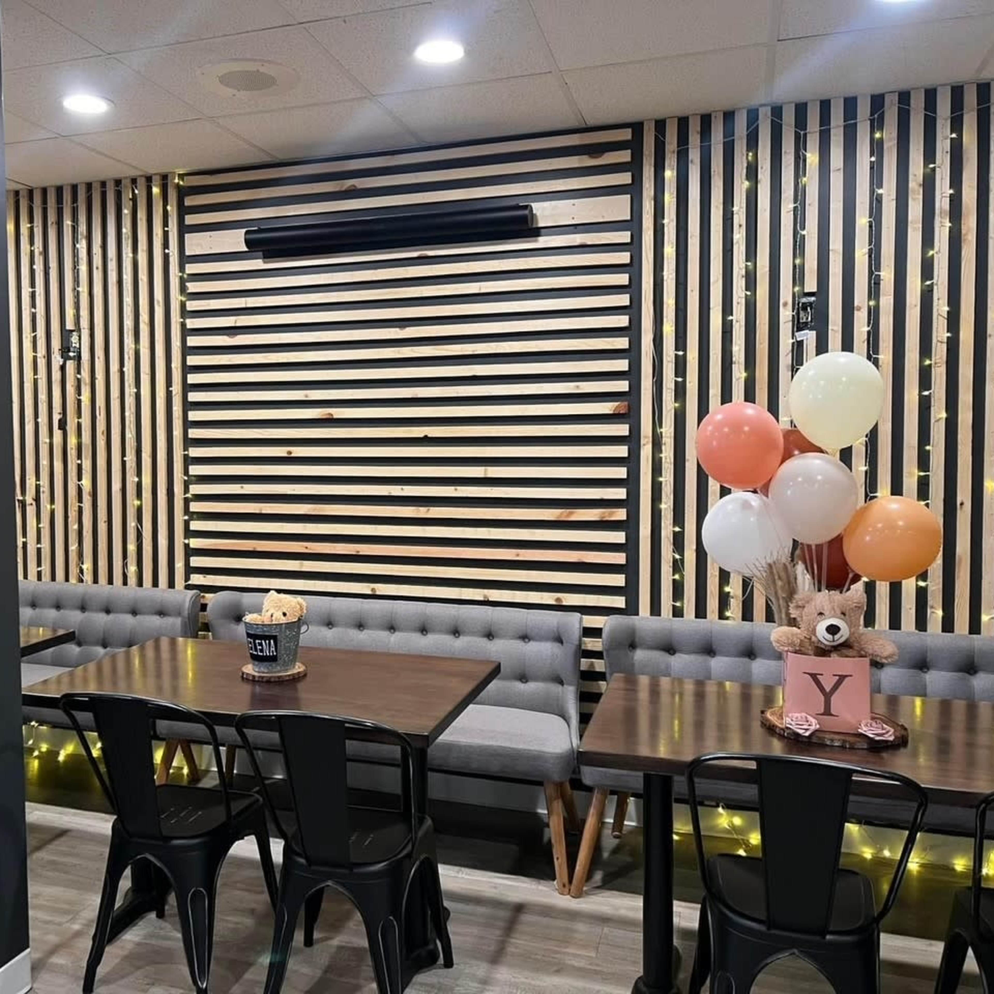 A modern cafe interior with wooden slat walls, gray upholstered seating, and tables arranged with decorative balloons on one side.