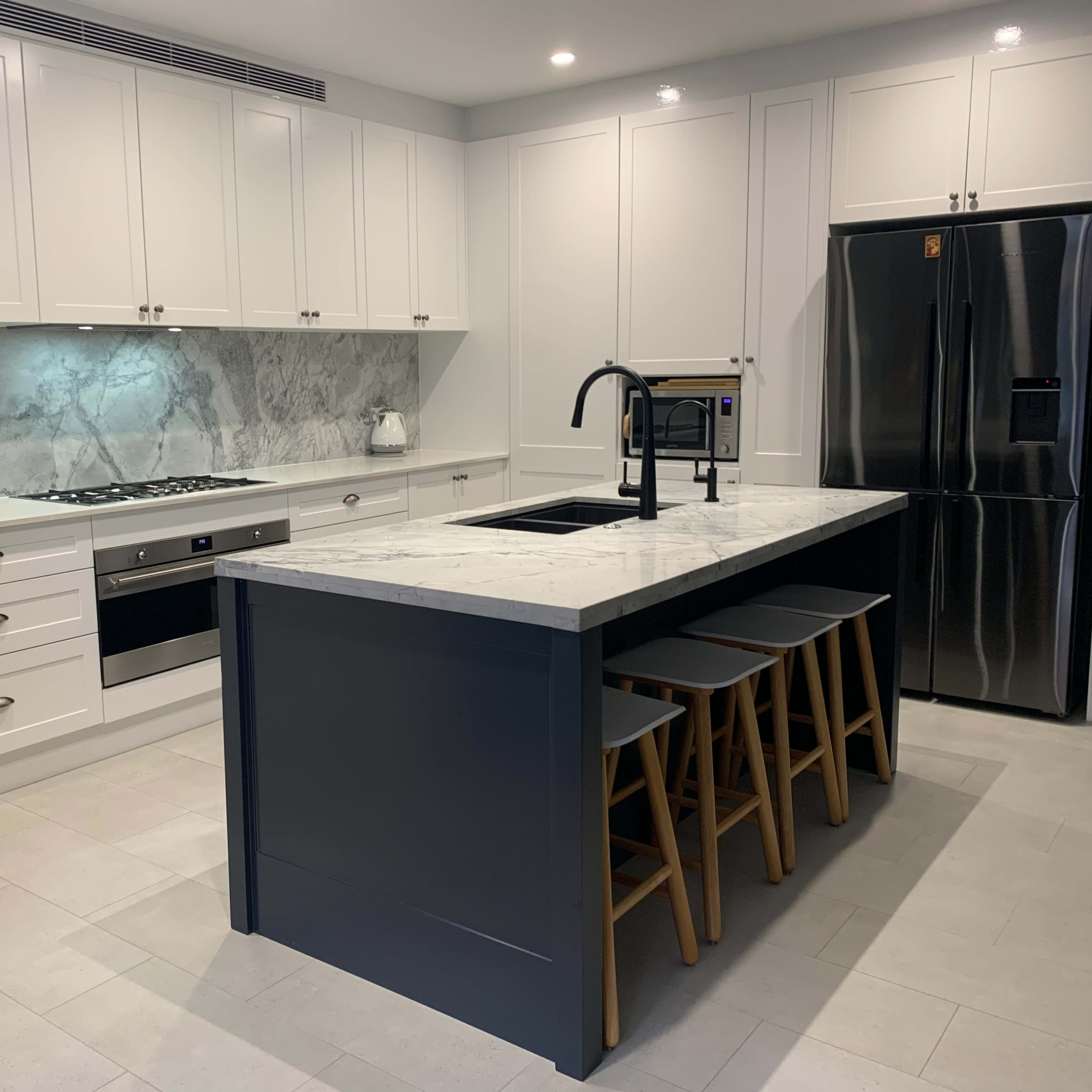 A modern kitchen featuring white cabinetry, a marble countertop island with three wooden stools, and stainless steel appliances.
