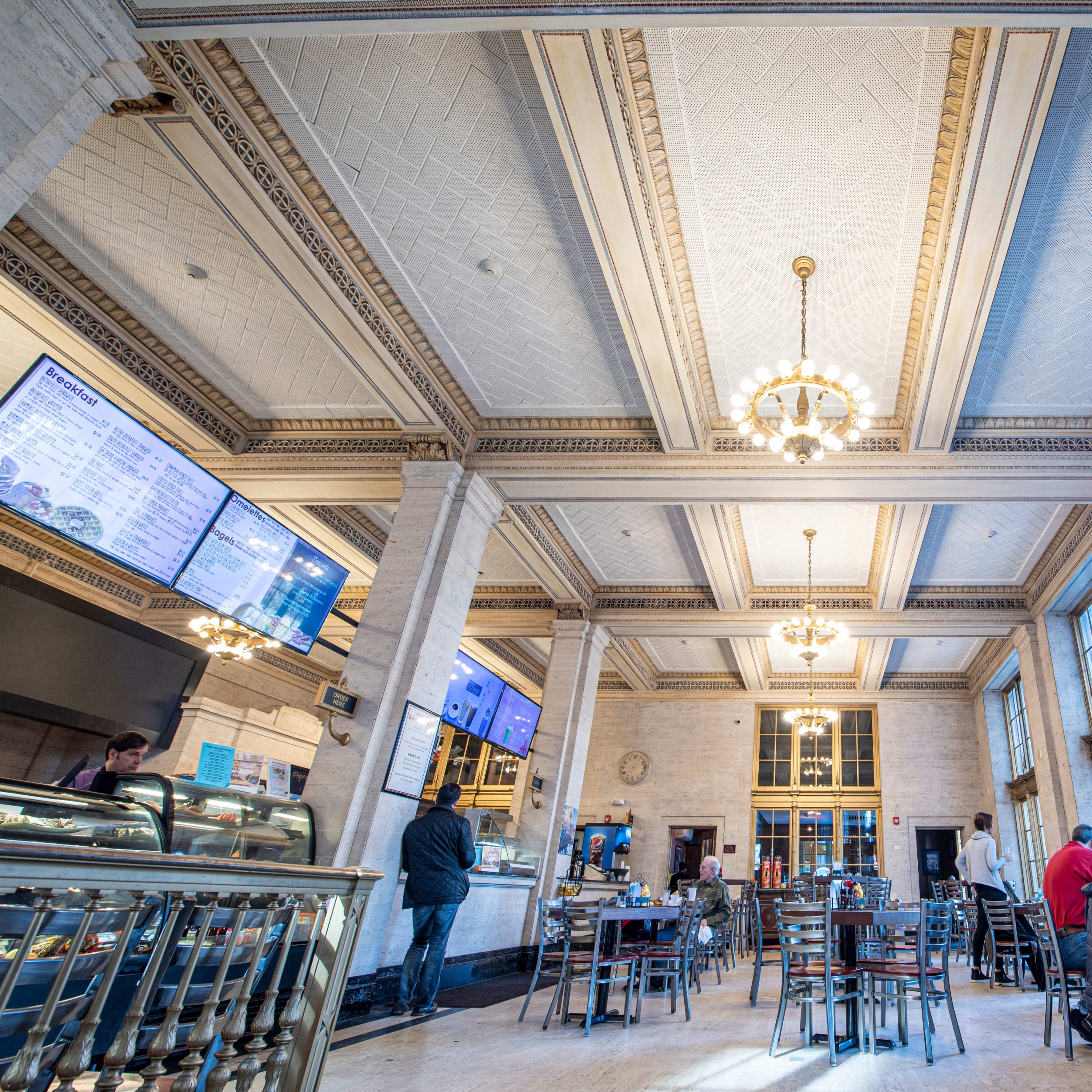 A spacious restaurant interior with high ceilings, large windows, and a mix of tables and chairs, occupied by a few patrons and staff.