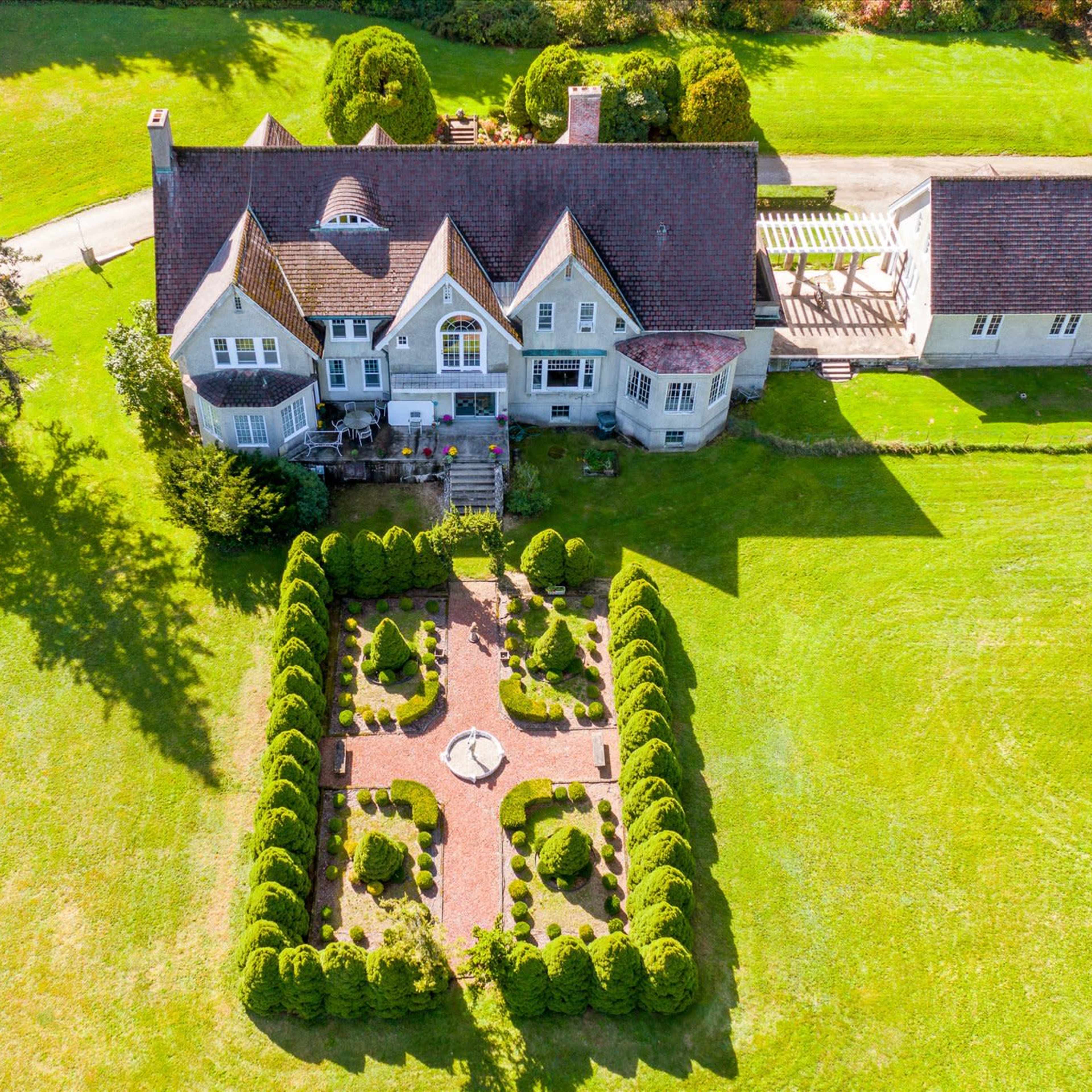 A large, multi-story house surrounded by manicured lawns and a formal garden with hedges and a central pathway.