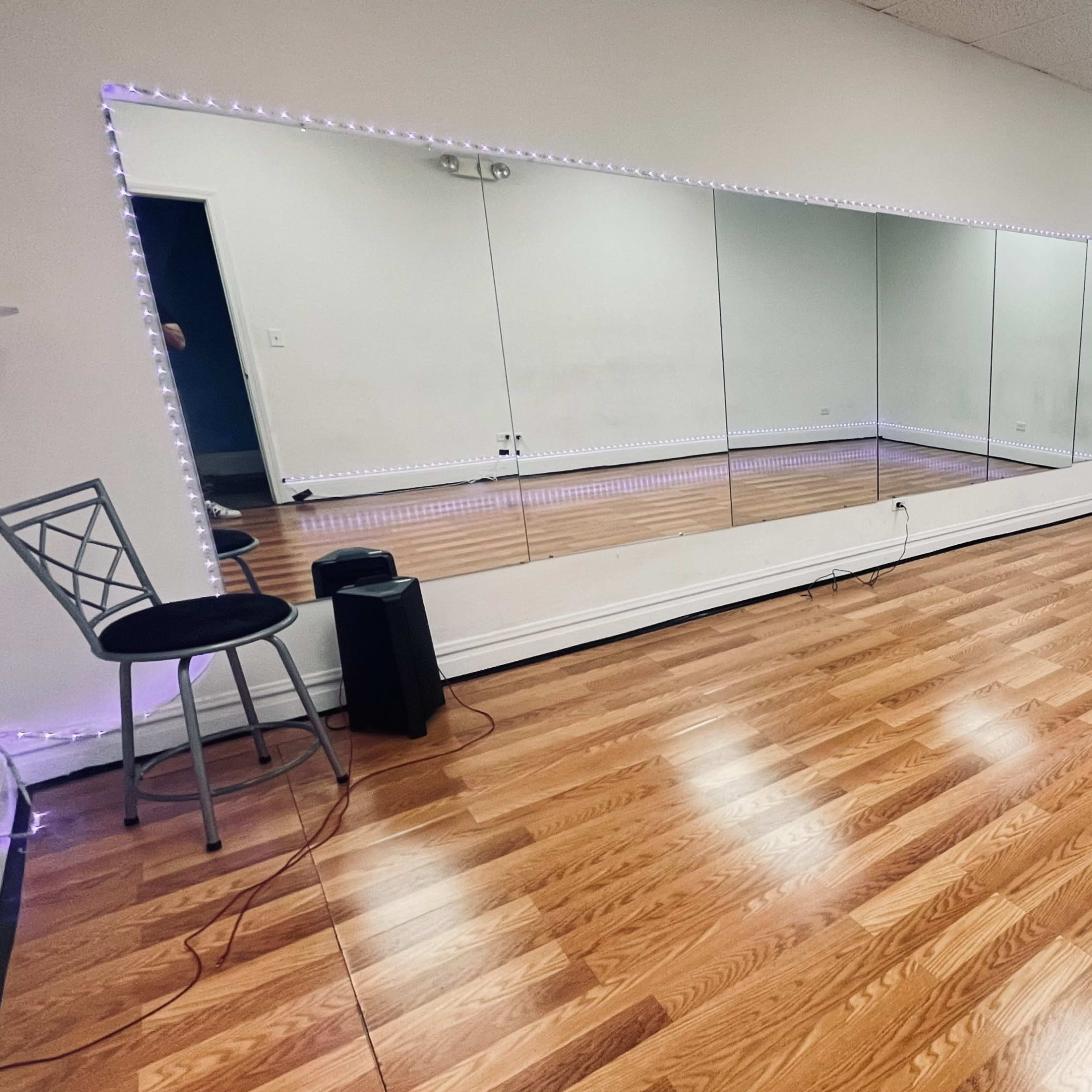 An empty dance studio with hardwood floors, a large mirror on one wall, and accent lighting along the edges.
