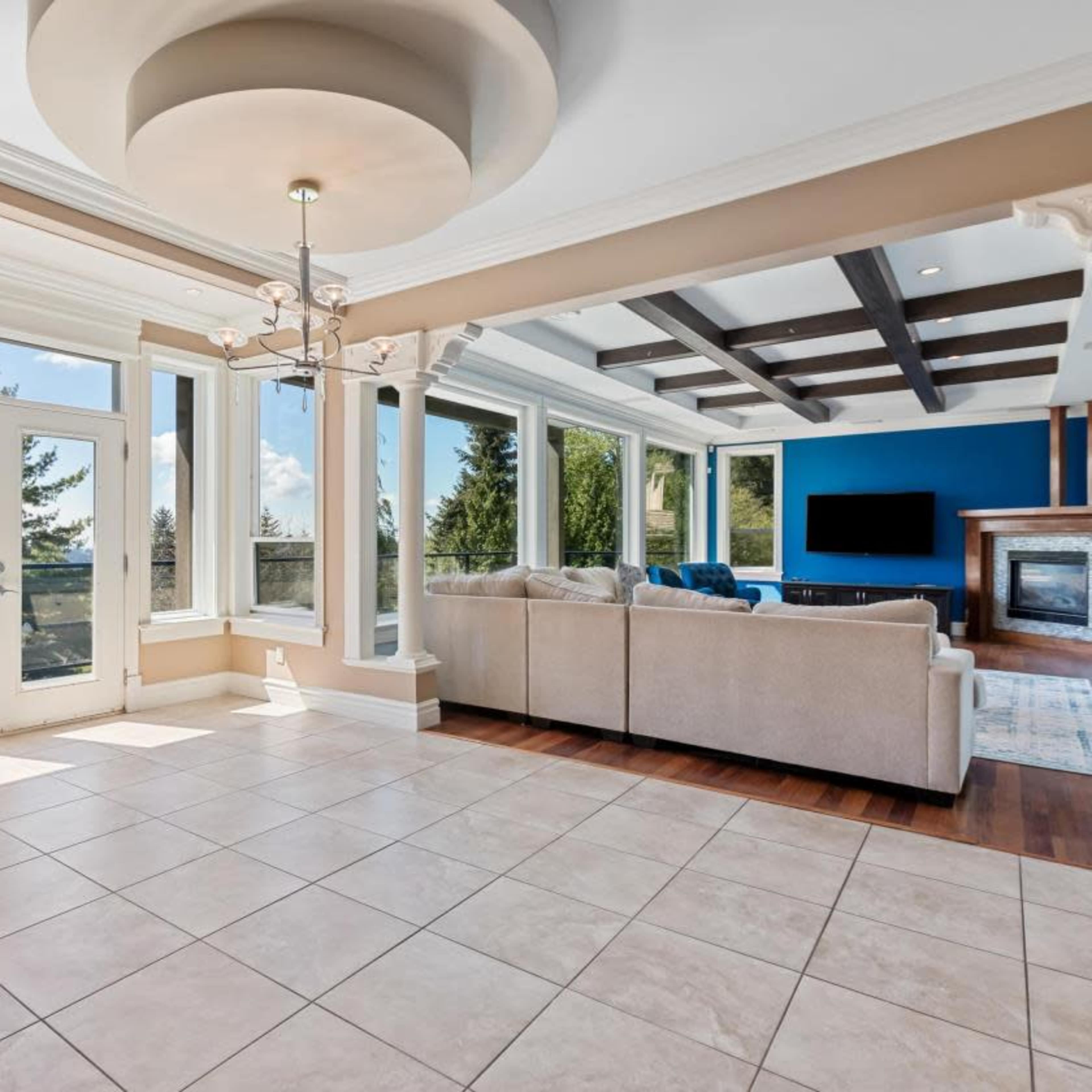 The interior of a spacious living room features large windows, a neutral color palette, and a combination of tiled and hardwood flooring.