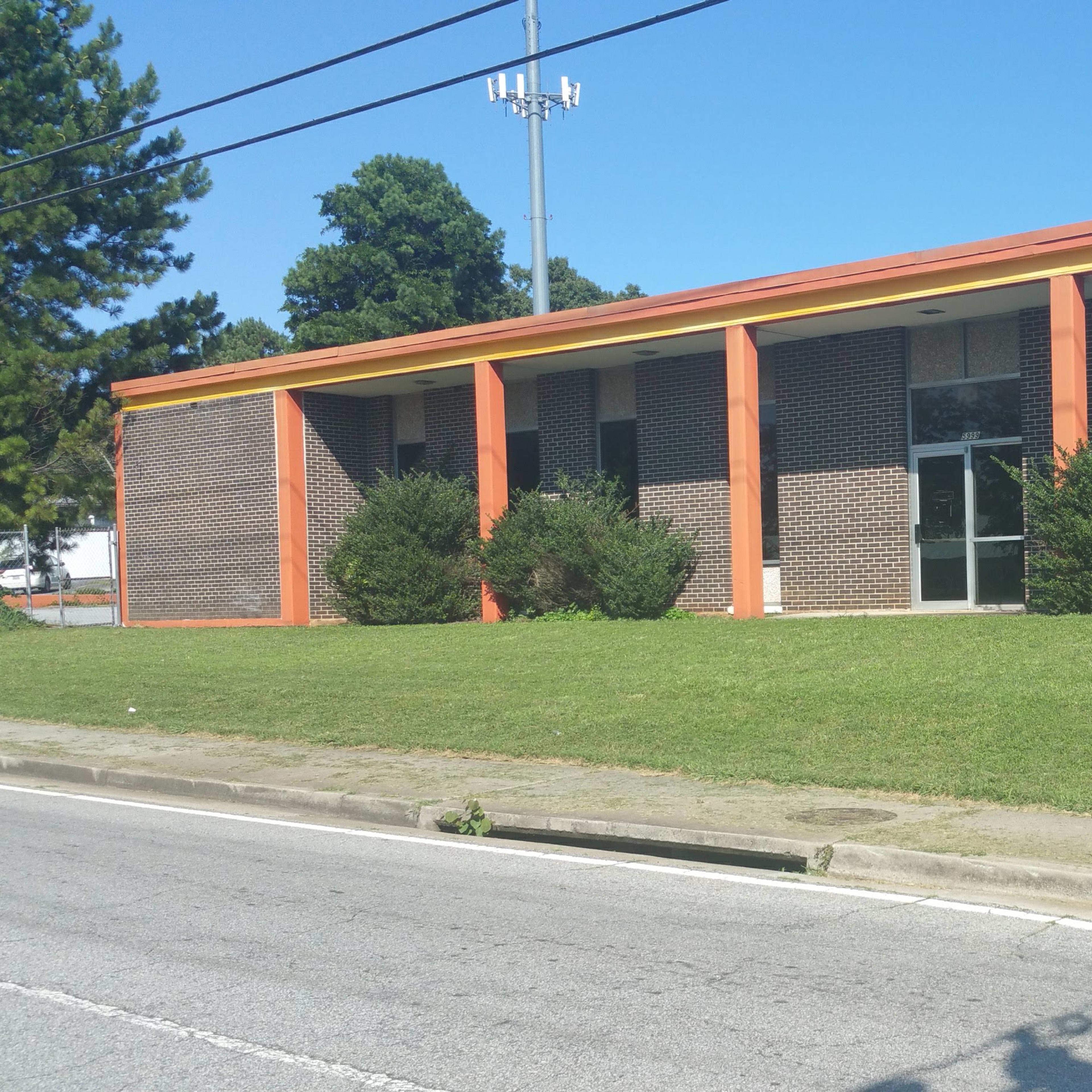 A single-story brick building with orange trim, situated on a grassy slope along a road.