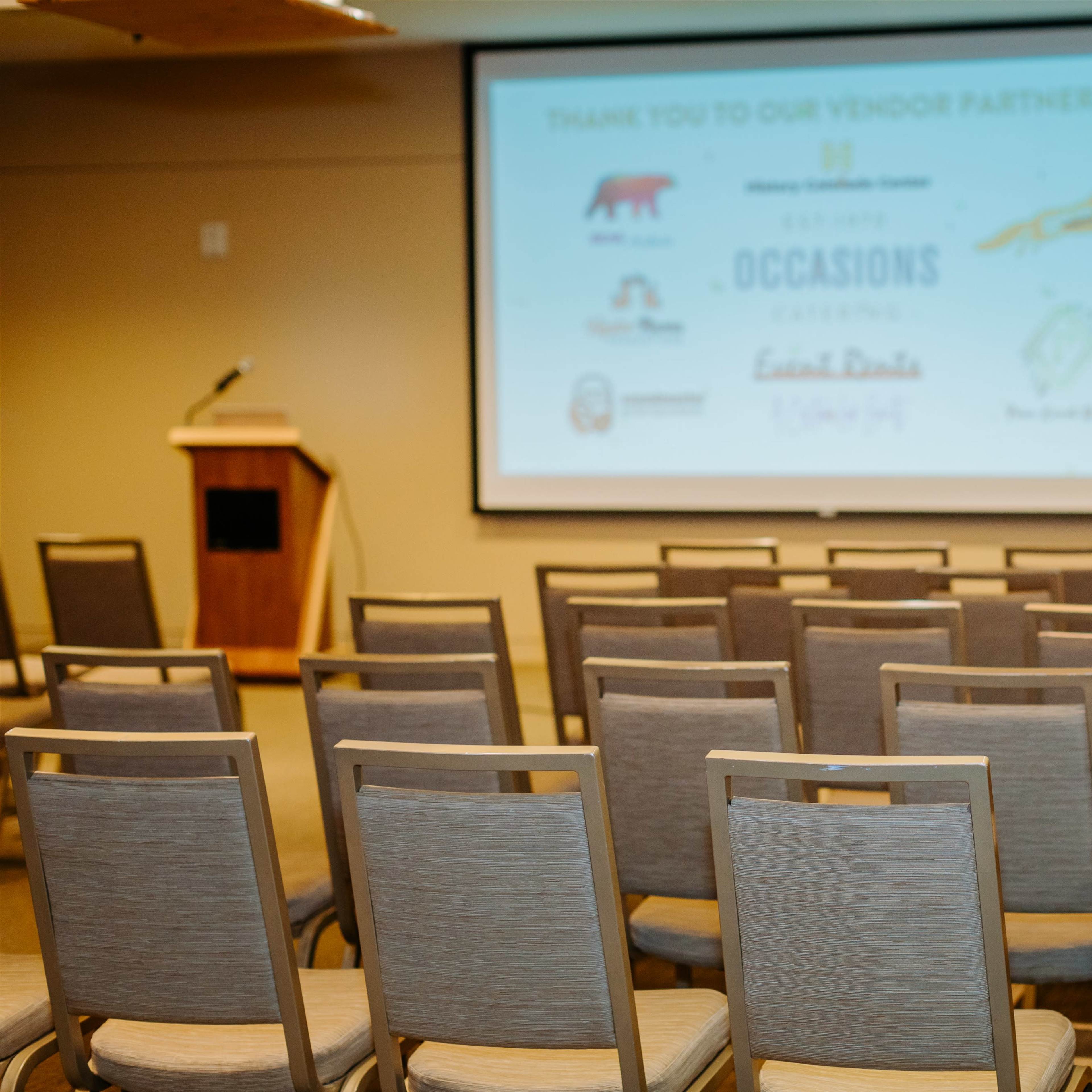 A conference room setup with rows of empty chairs facing a large screen displaying logos and a thank-you message to vendor partners.