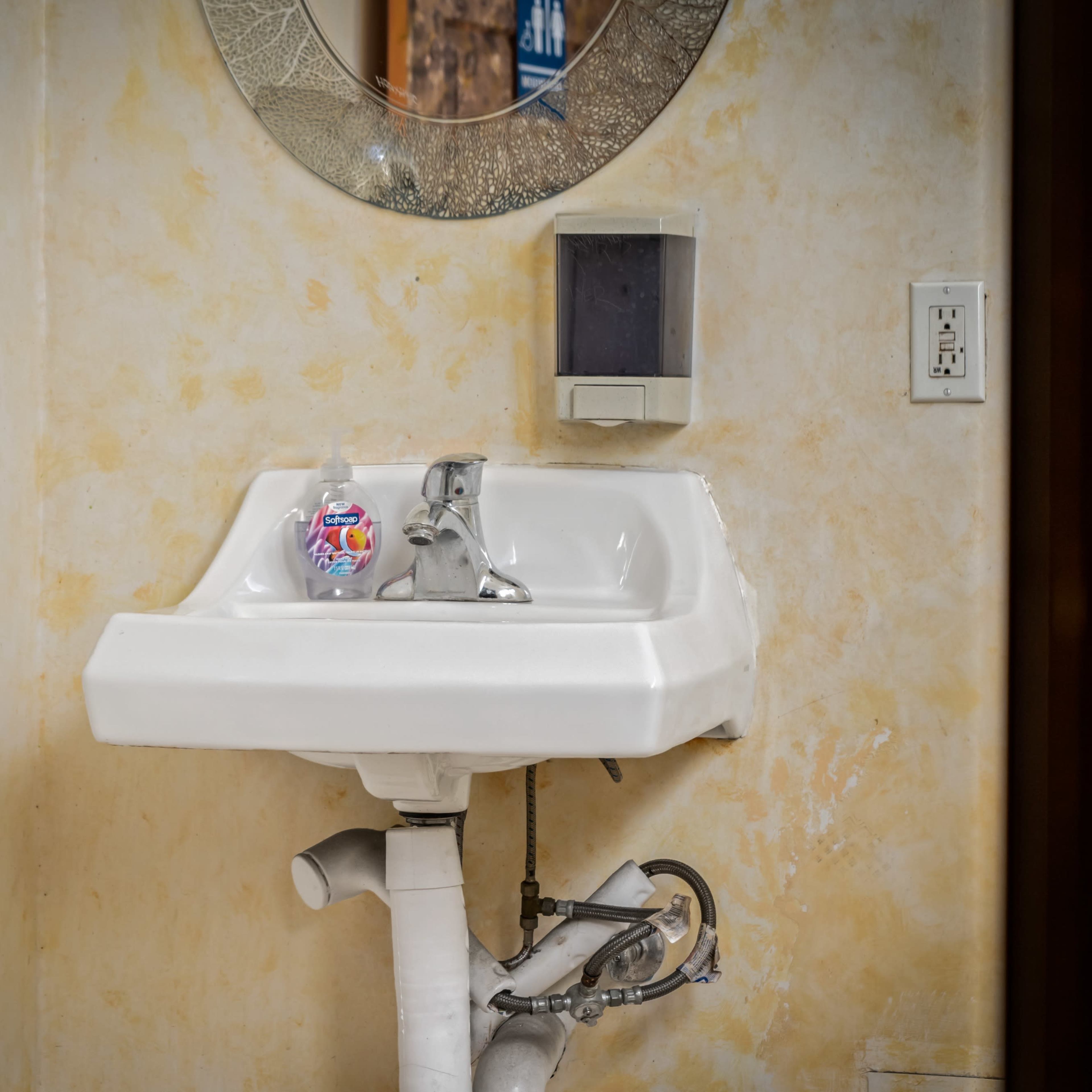 A small white sink mounted on a wall, featuring a mirror above it and a soap dispenser to the side.