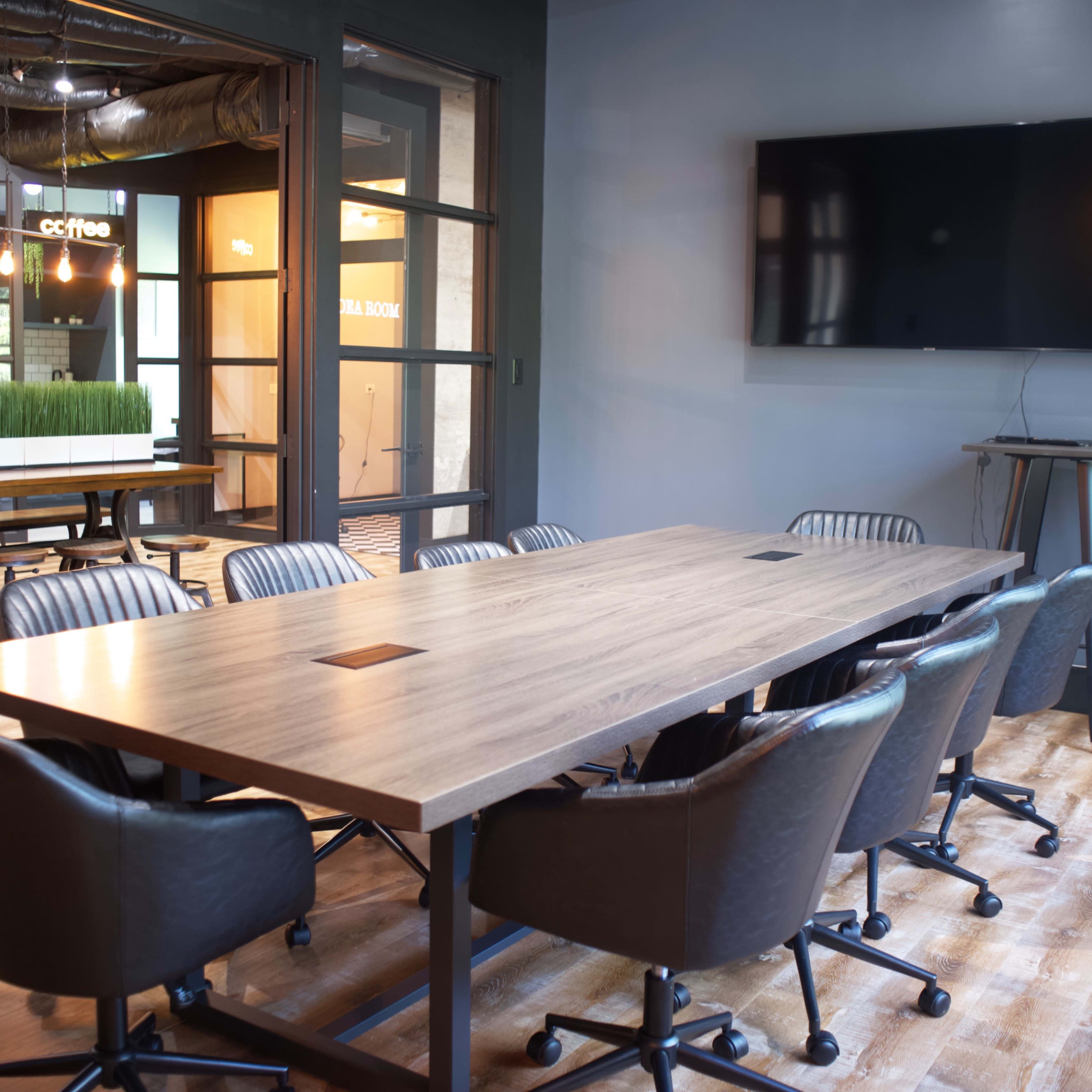 A modern conference room features a large wooden table surrounded by ergonomic chairs and a wall-mounted television.