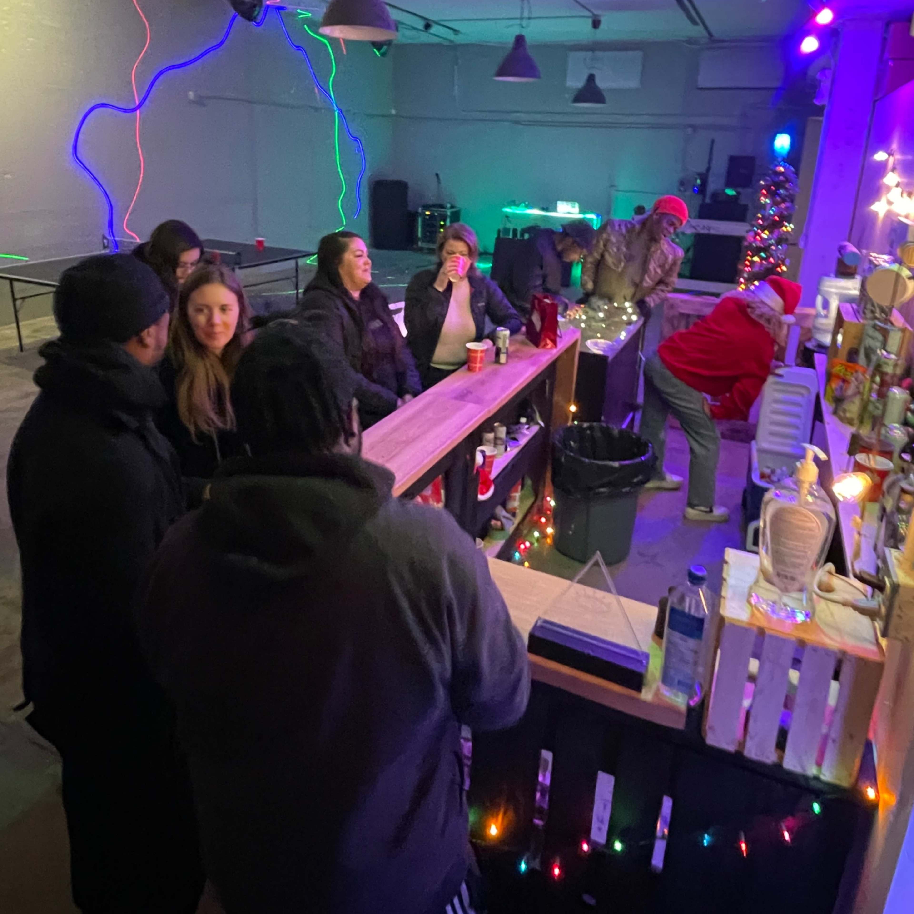 A group of people gather at a bar area decorated with colorful lighting and festive decorations.