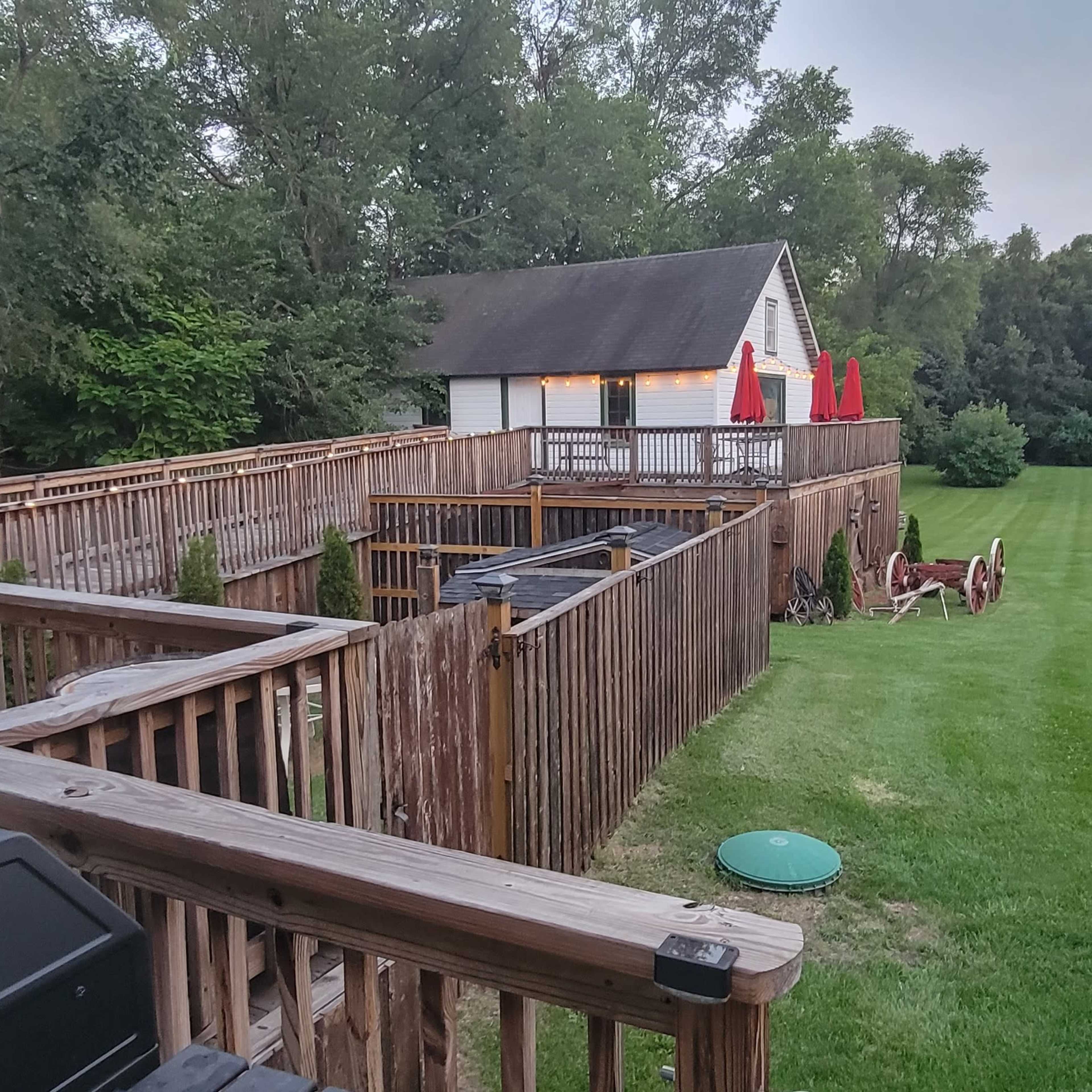 A wooden deck overlooking a grassy backyard with a fenced area, a storage shed, and a large white tent set up for an event.