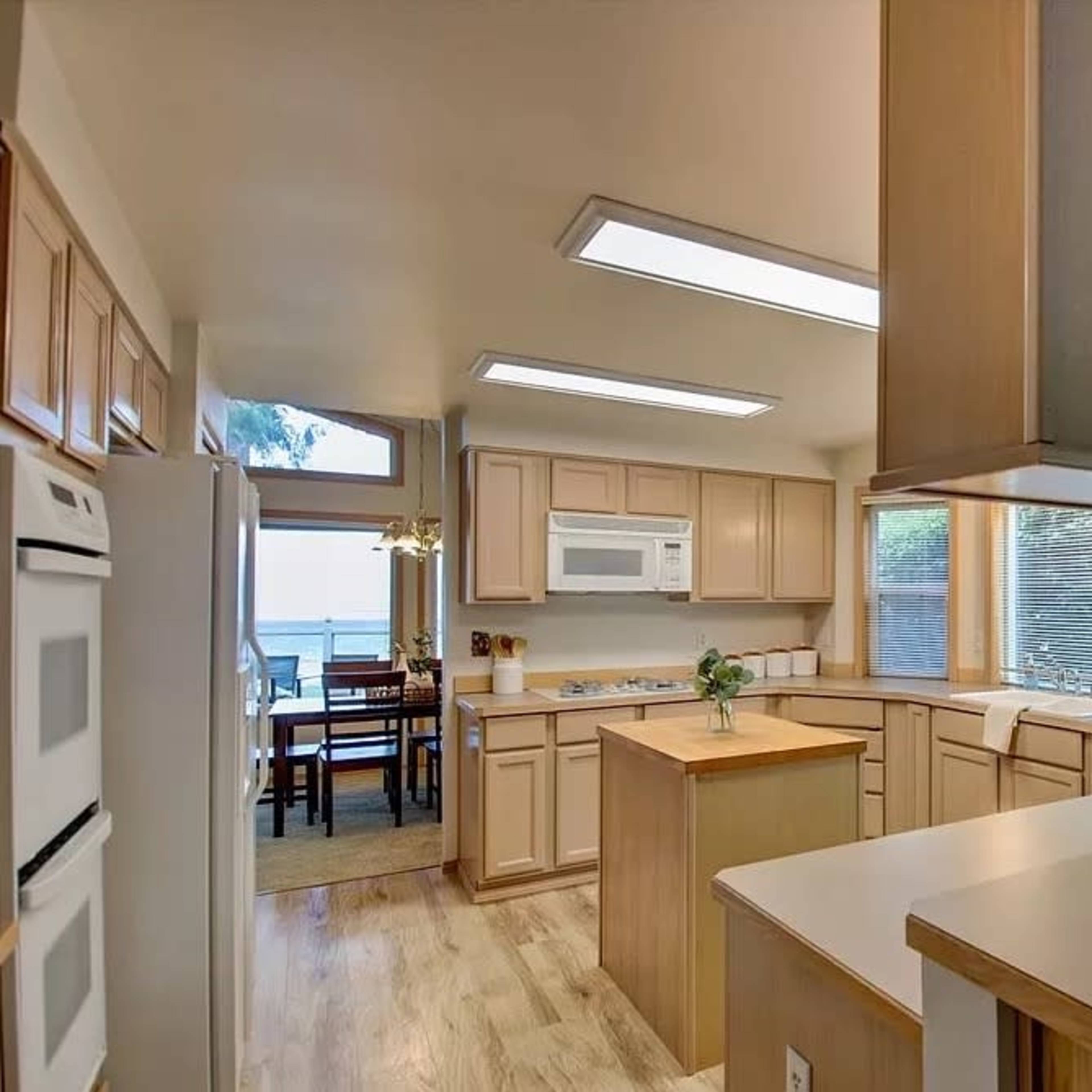A spacious kitchen features wooden cabinetry, a central island, and large windows allowing natural light to enter.