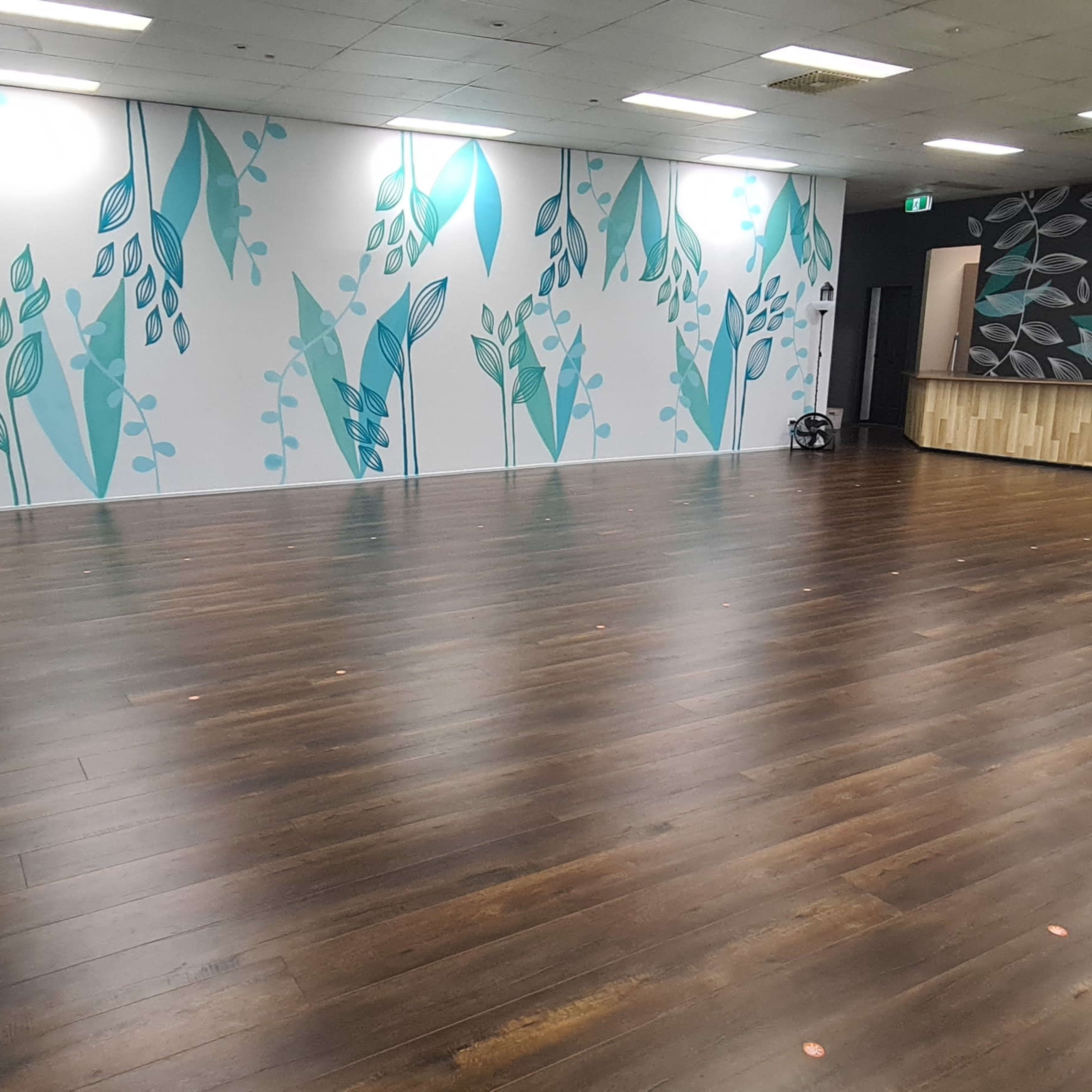 A spacious room with wooden flooring and walls decorated with blue and green leaf patterns.