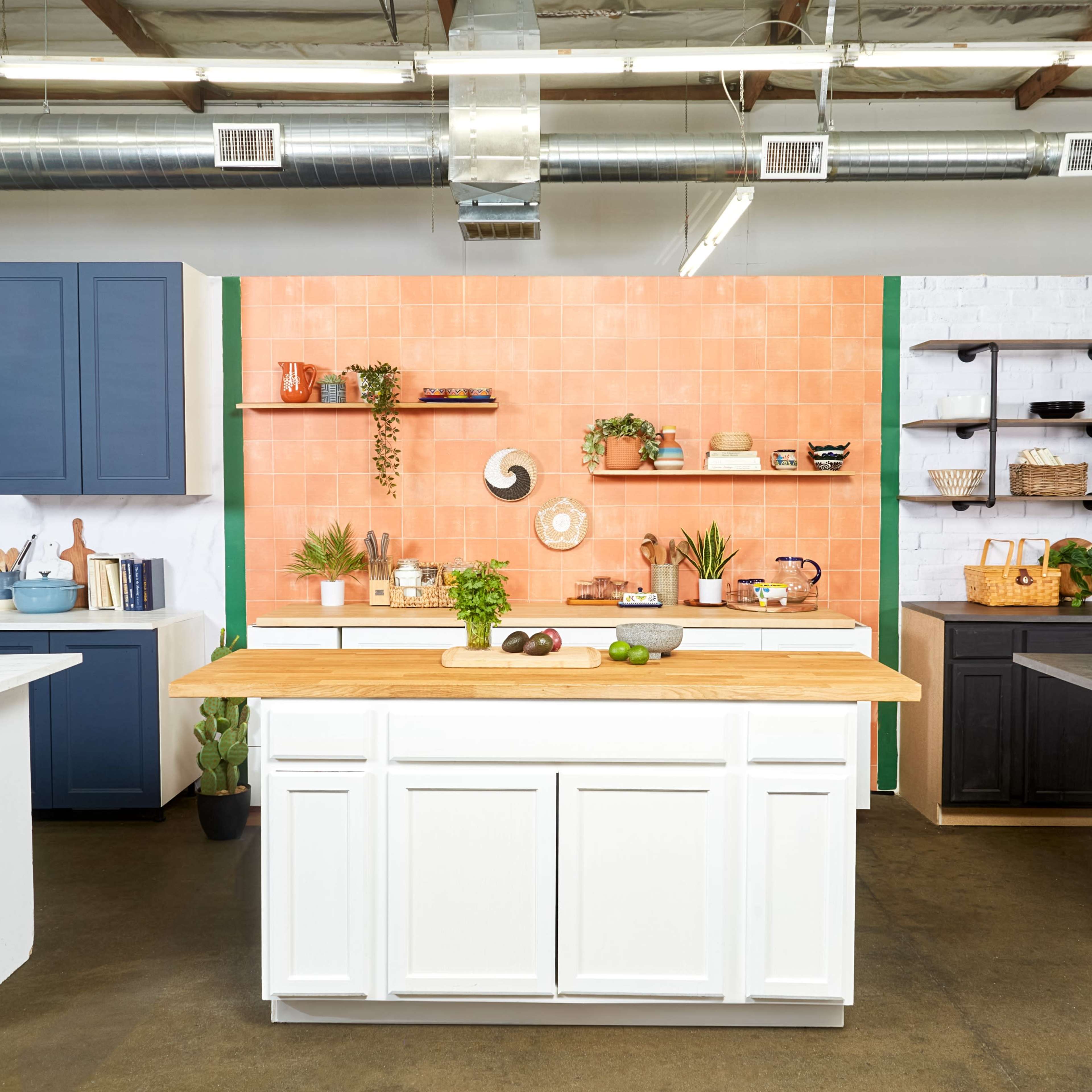 A modern kitchen setup featuring multiple islands and cabinets in various colors, with open shelving displaying kitchenware and plants against a tiled backdrop.