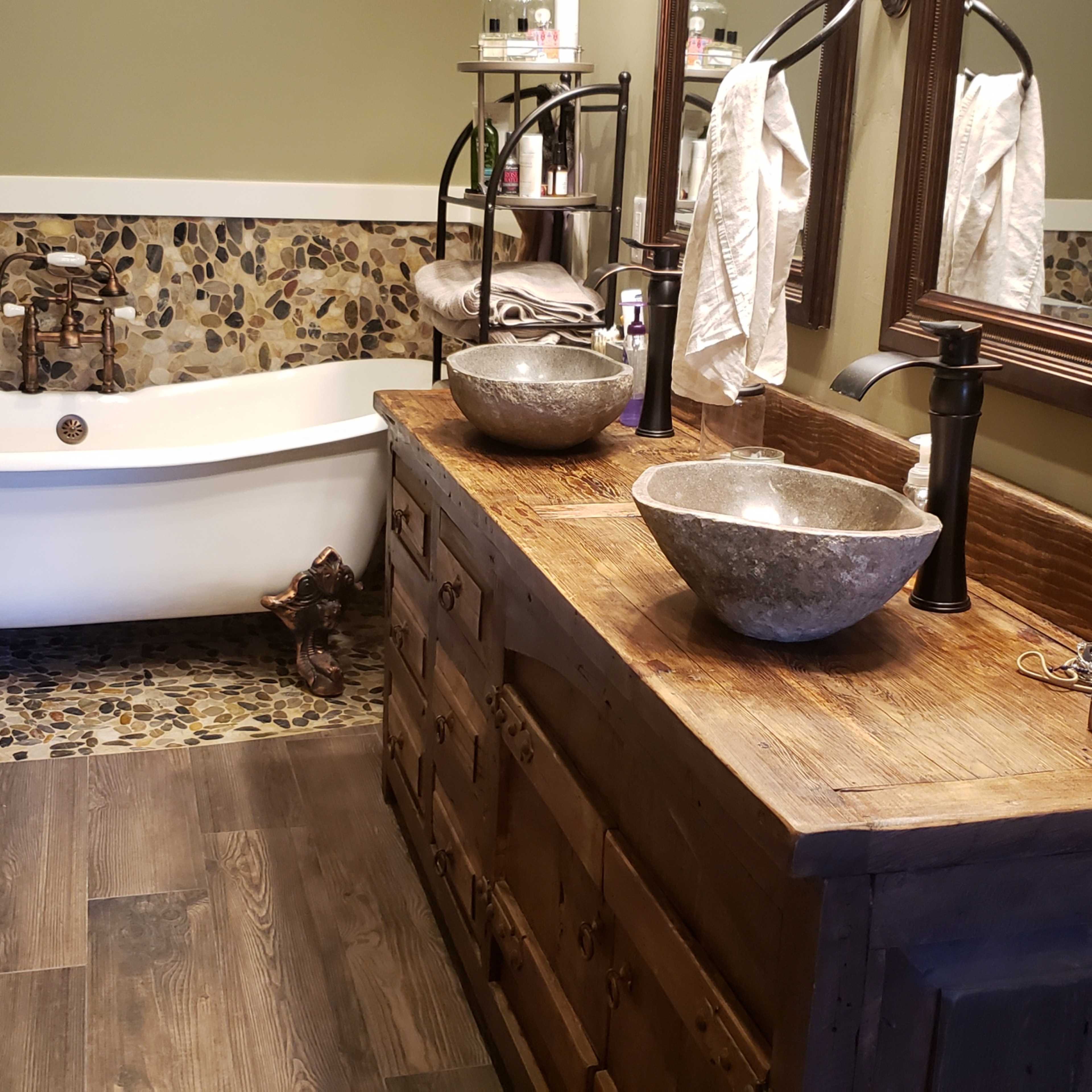 A bathroom featuring a clawfoot bathtub, a wooden vanity with stone sinks, and a pebbled wall trim.