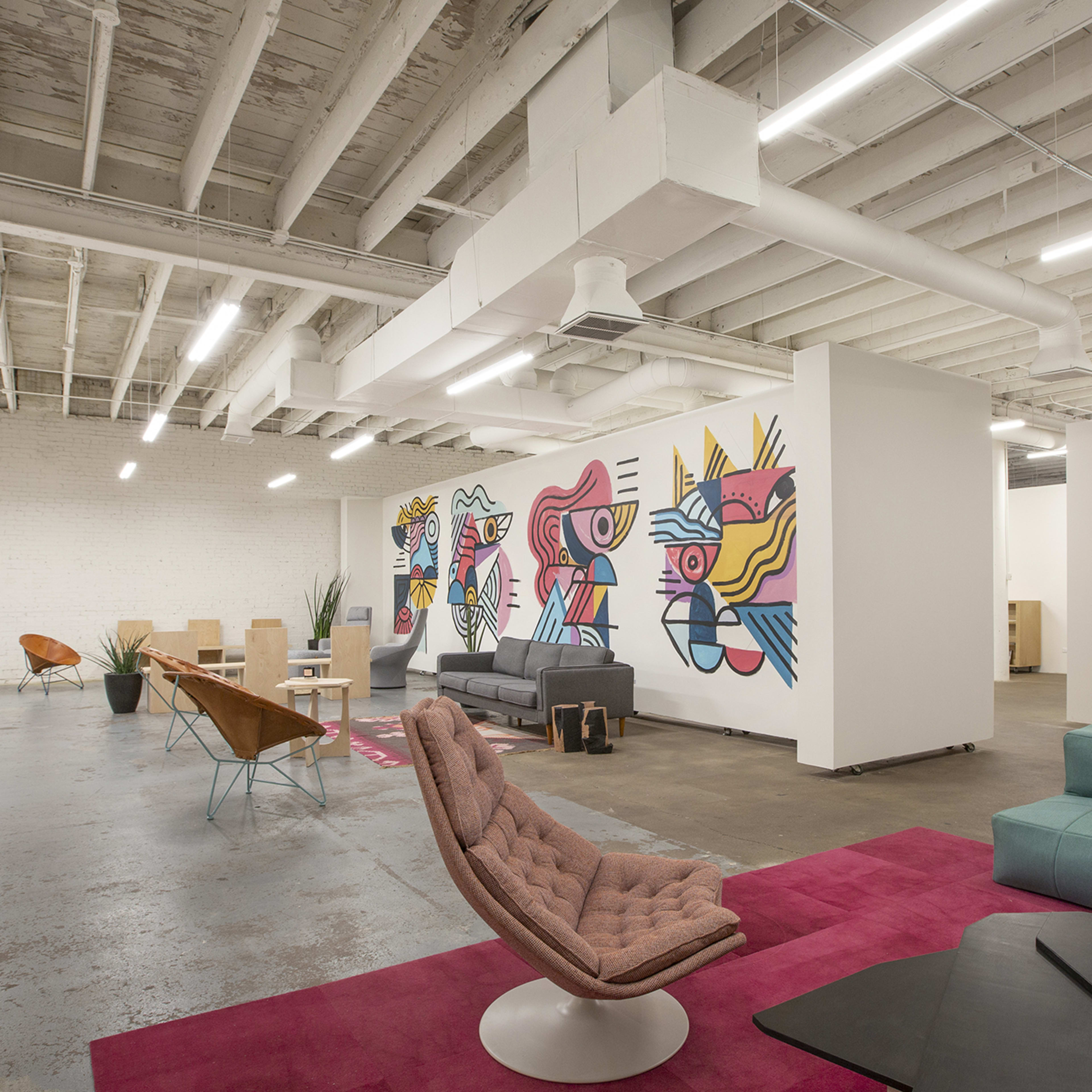 An open office space with modern furniture, colorful wall murals, and a mix of seating arrangements.