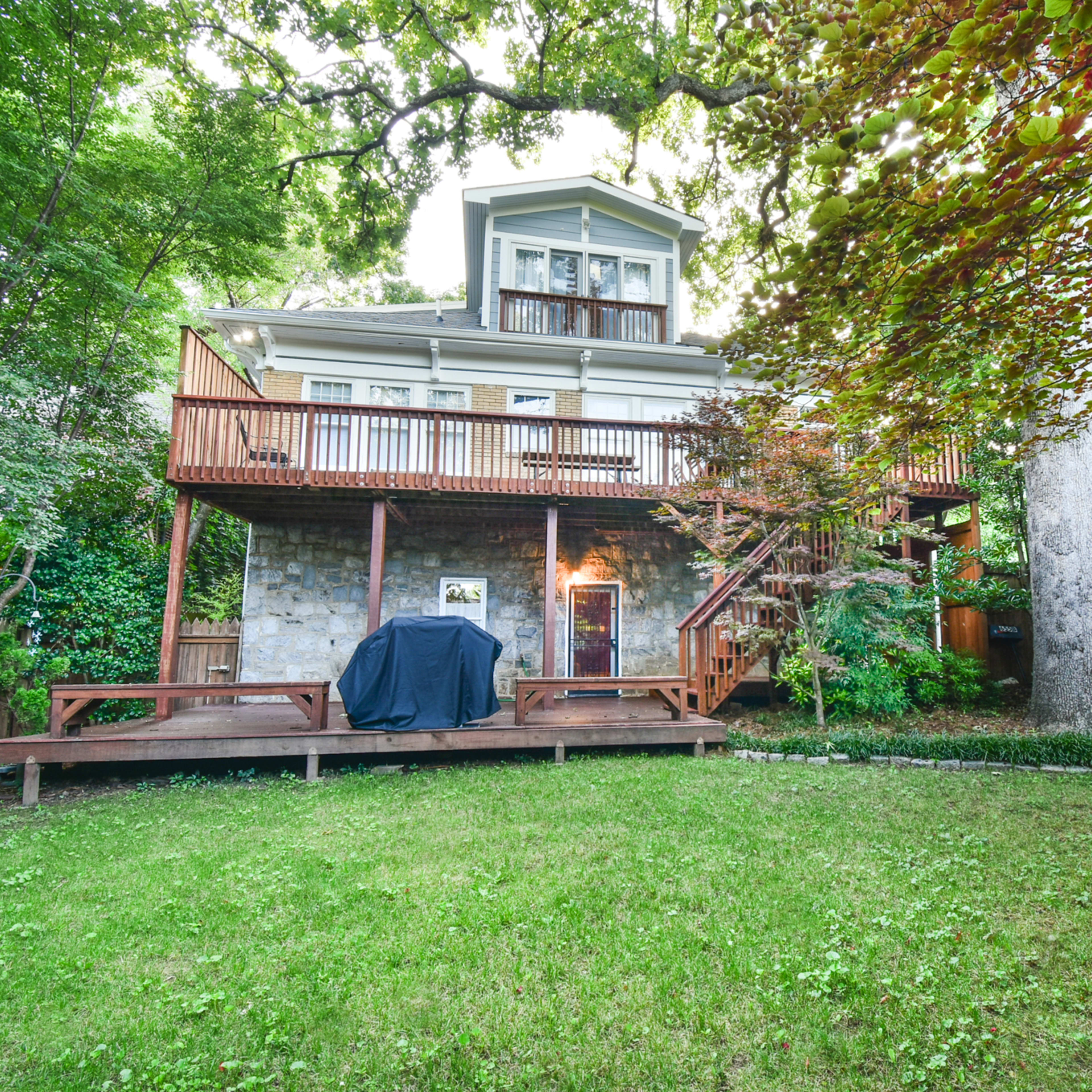 A multi-level house with a large wooden deck in the backyard, surrounded by trees and greenery.